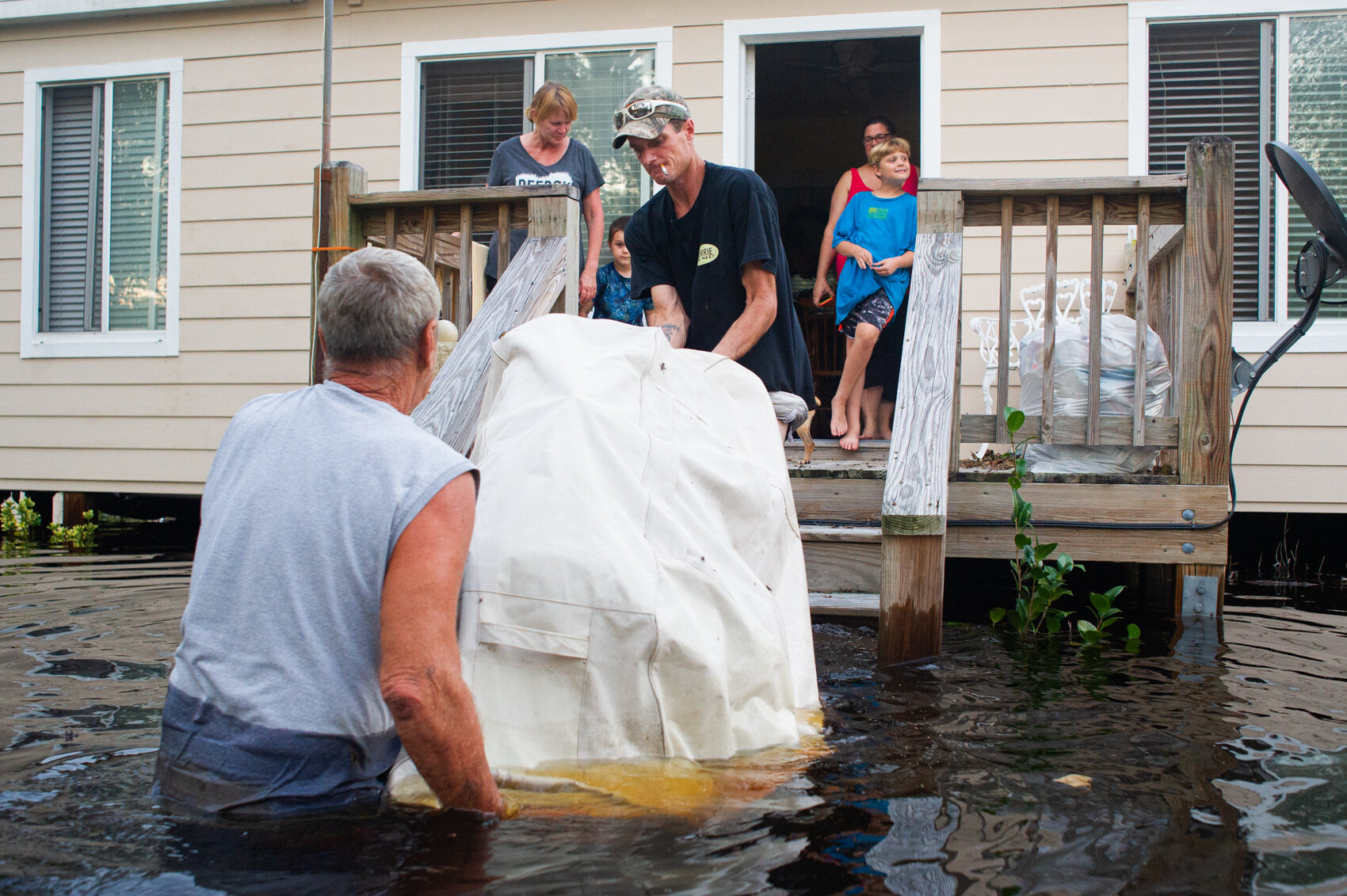  Mike Hicks, left, helps lift his grill onto his back porch in a flooded neighborhood on Alexis Hales Road near the Black River in Currie, North Carolina on Wednesday evening, September 19, 2018. (Port City Daily photo | Mark Darrough) 