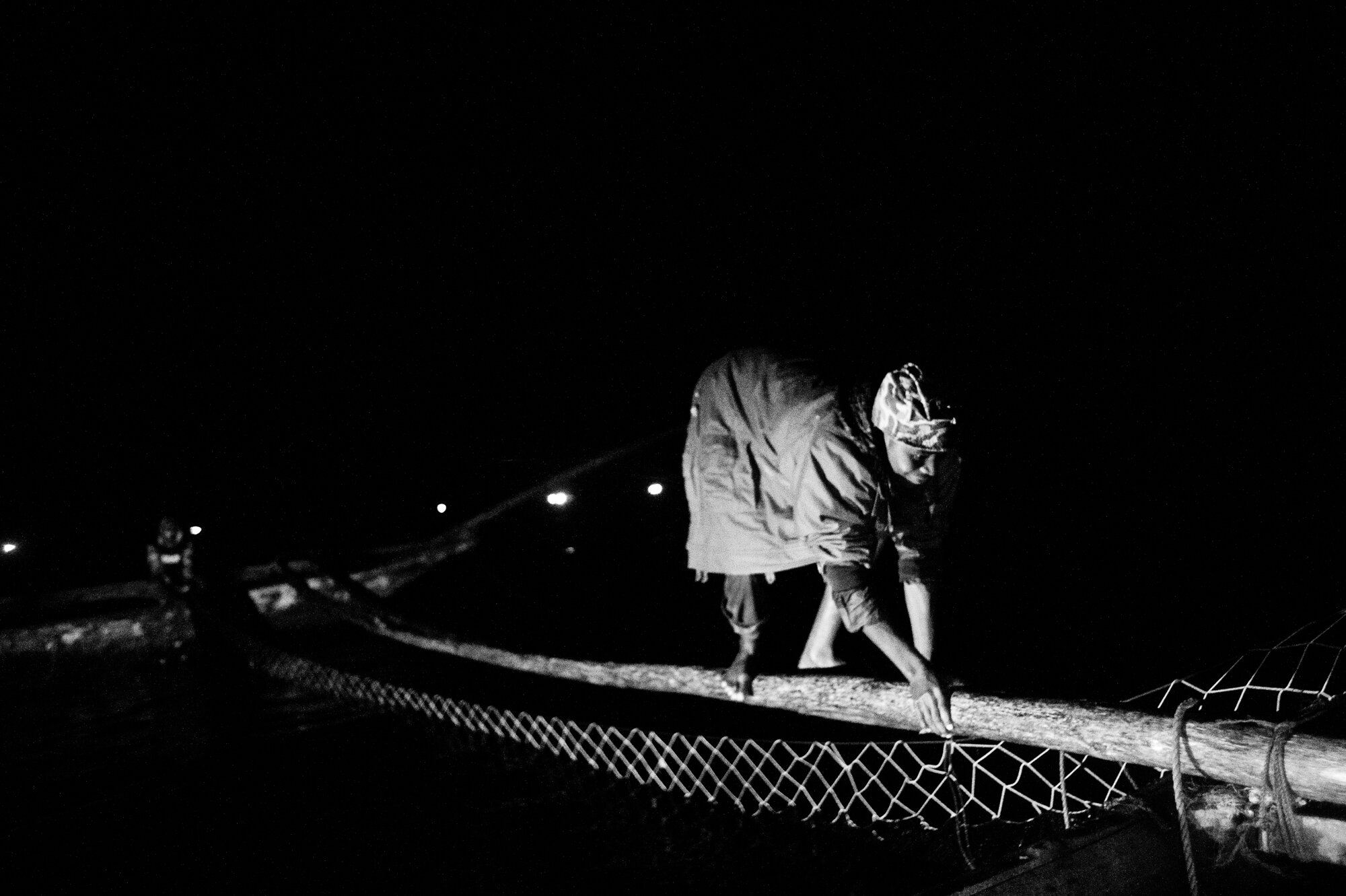  A fisherman balances on a piece of eucalyptus strung between two wooden boats as his crew pulls up sambaza-filled nets hung between the boats. 