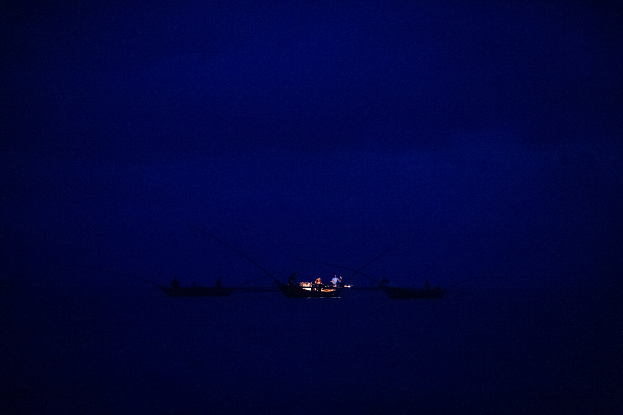  Fishermen in clusters of three wooden boats hang lanterns to draw sambaza (“lake sardines”) to the surface on a moonless night, Lake Kivu, Rwanda. 