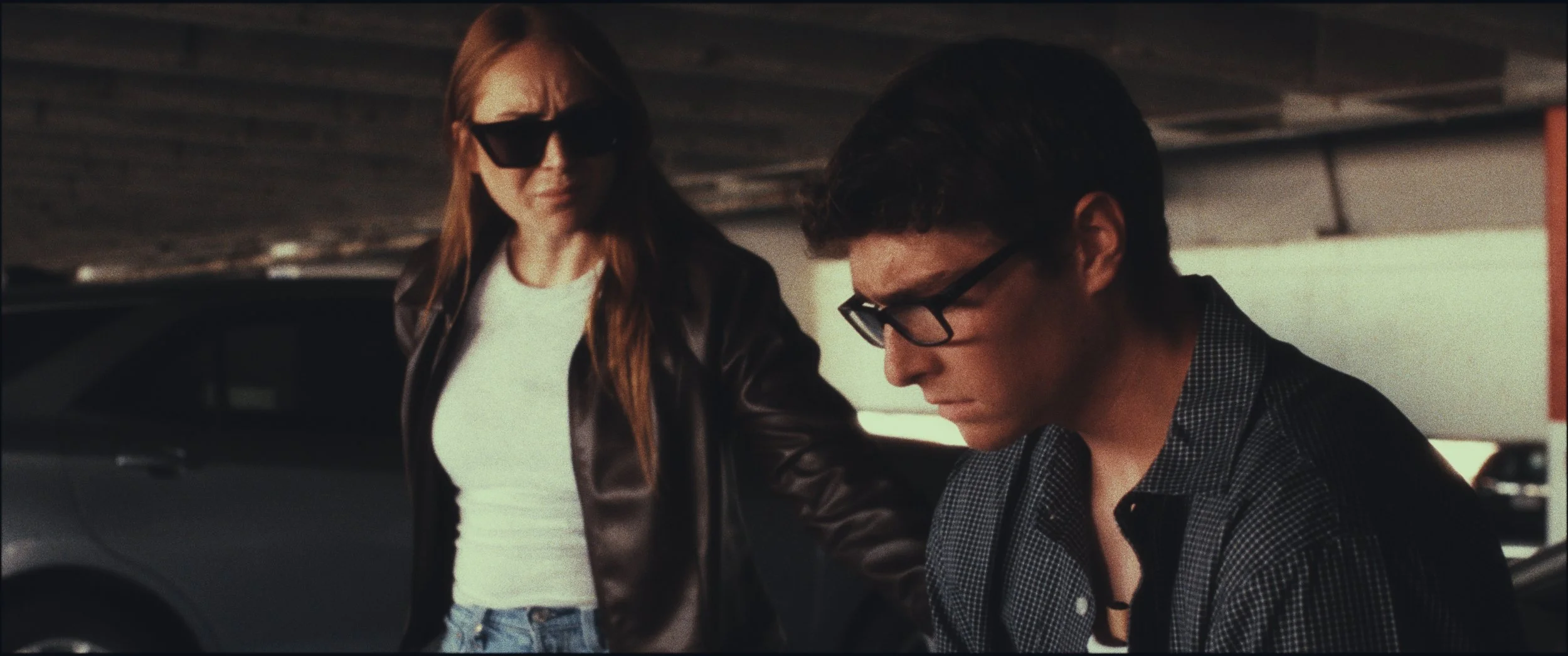 A woman in sunglasses and a man in glasses in a parking garage, still from Five Finger Stakeout (2026), shot in Omaha, Nebraska by cinematographer Cole Mowery