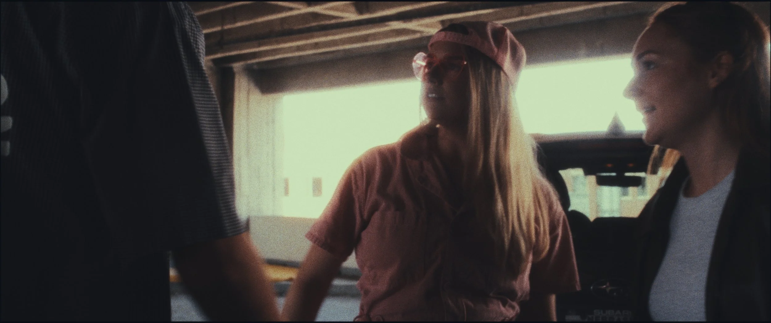 Woman in a pink cap talking with another woman in a parking garage, still from the short film Five Finger Stakeout (2026)