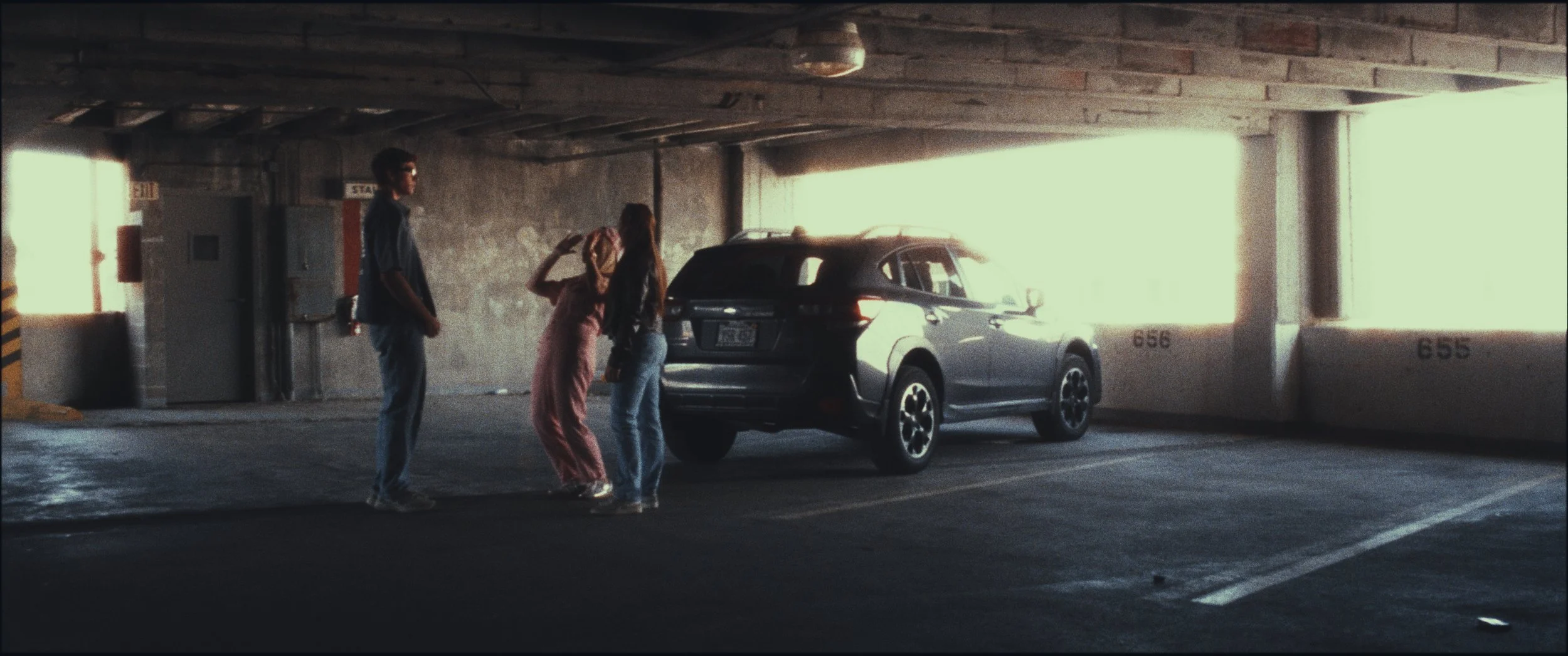 Wide shot of three people standing beside an SUV in a parking garage, still from the short film Five Finger Stakeout (2026)