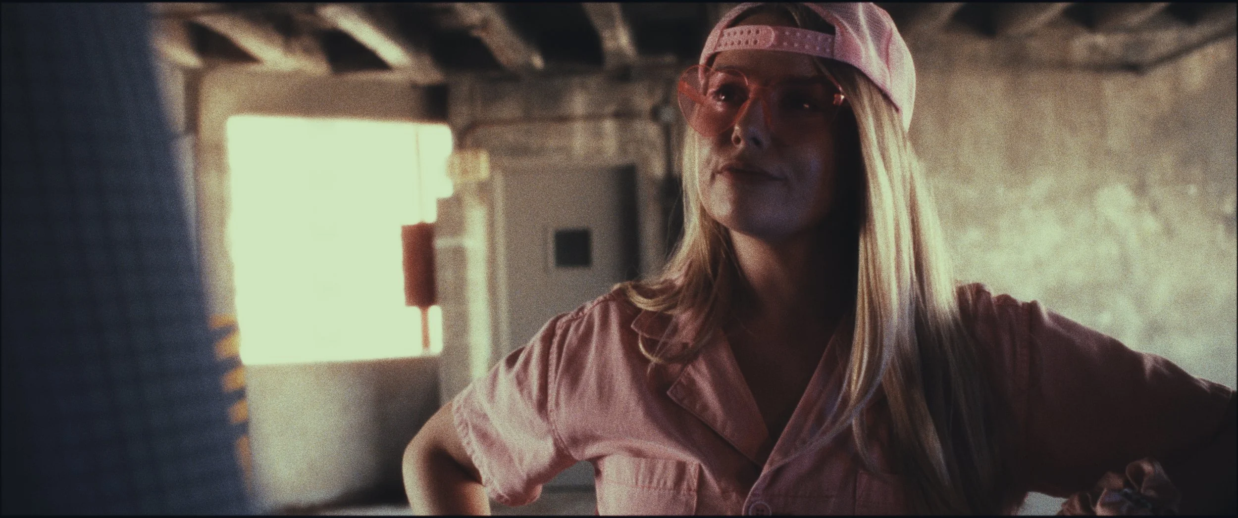 Woman in a pink cap and pink shirt in a parking garage, still from the short film Five Finger Stakeout (2026)