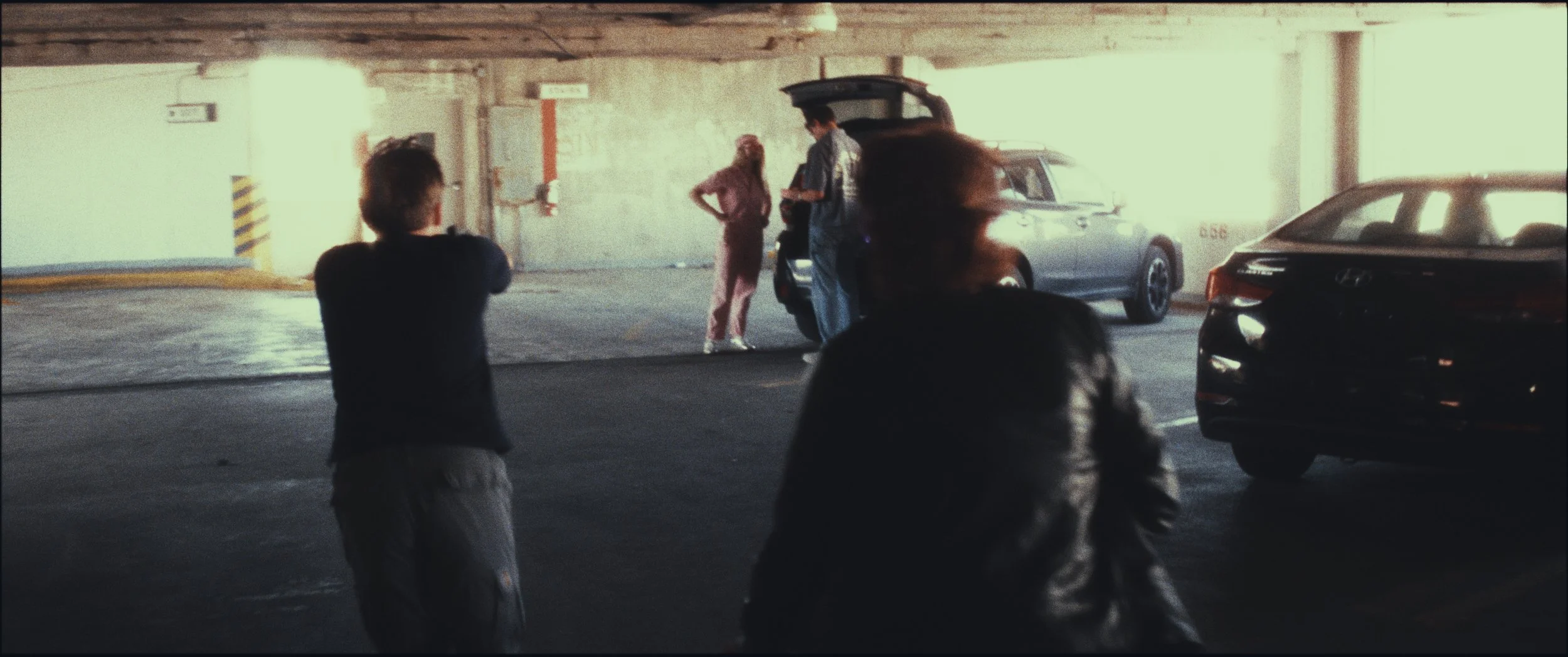 Wide shot of a standoff beside a car in a parking garage, still from the short film Five Finger Stakeout (2026)