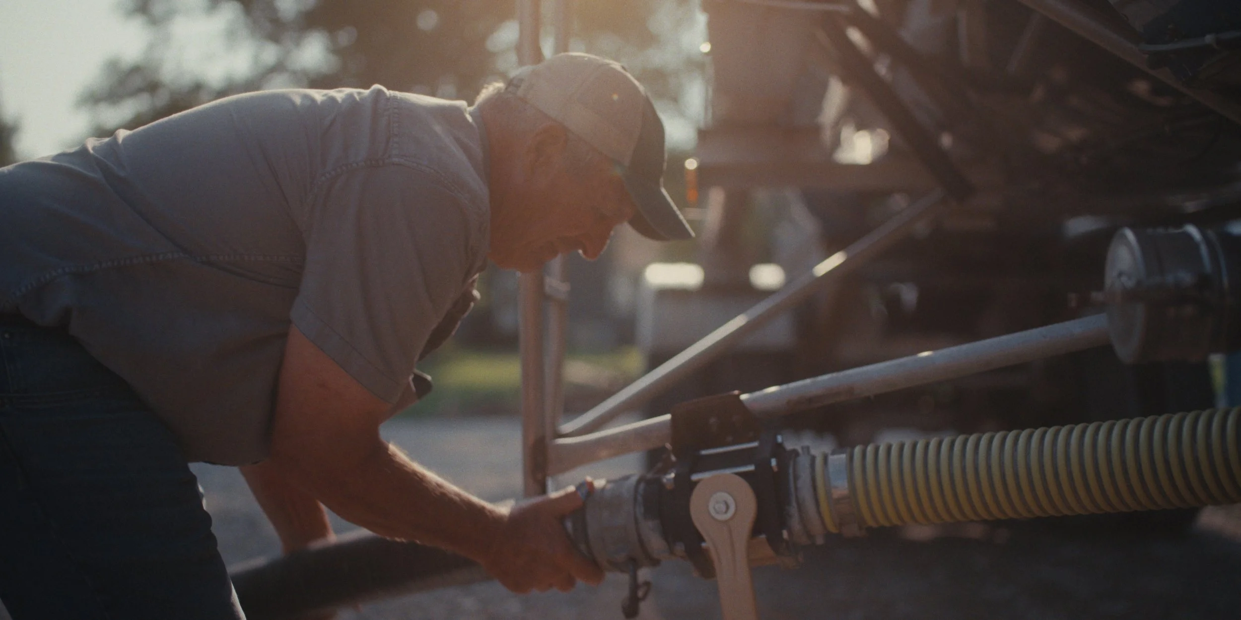 Farmer connecting a hose to farm equipment in warm backlight, still from a Folsom Lake Solar commercial shot in Mills County, Iowa by director of photography Cole Mowery