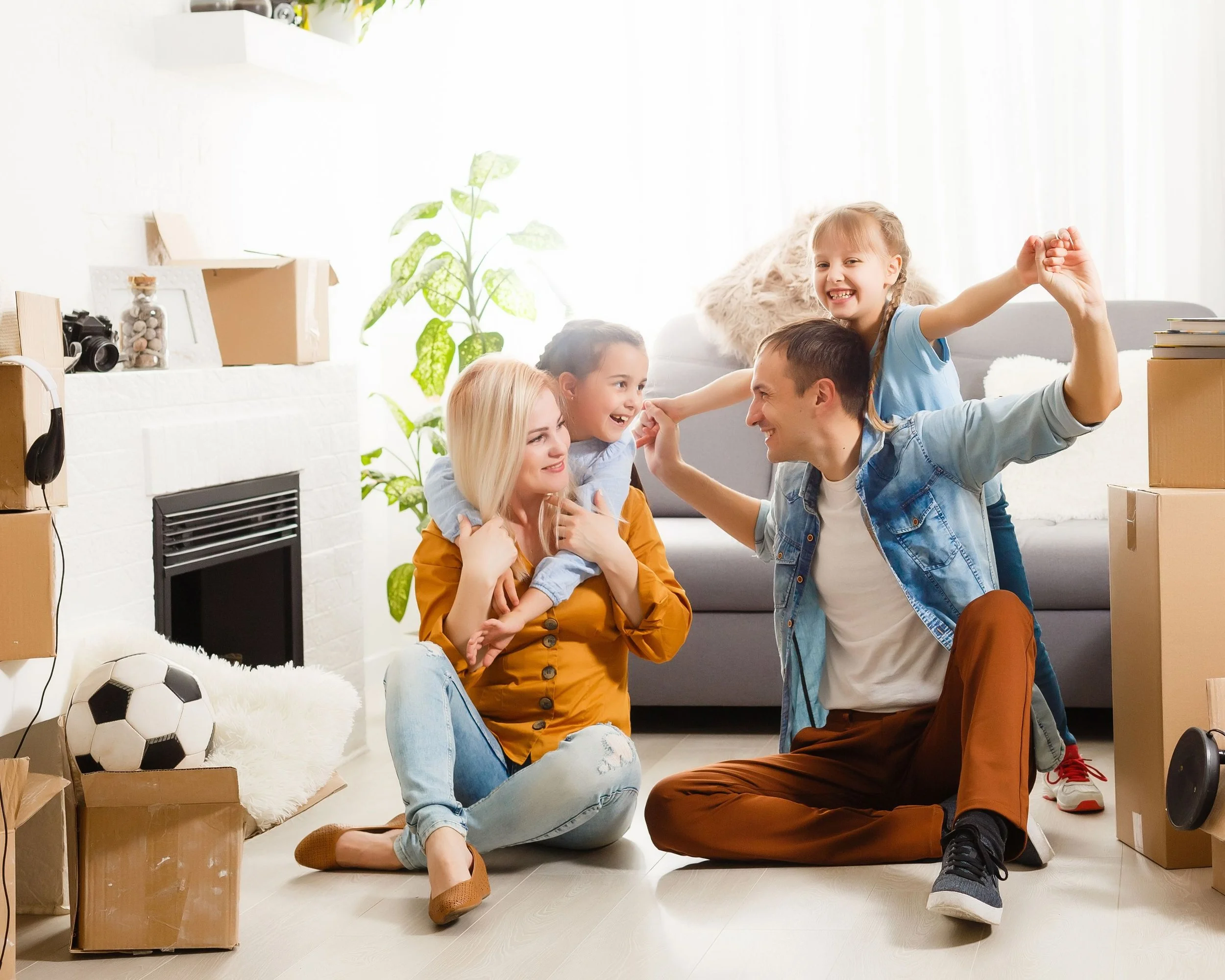 Una famiglia felice con due bambini che giocano e si abbracciano in soggiorno con scatole di trasloco e un pallone da calcio.