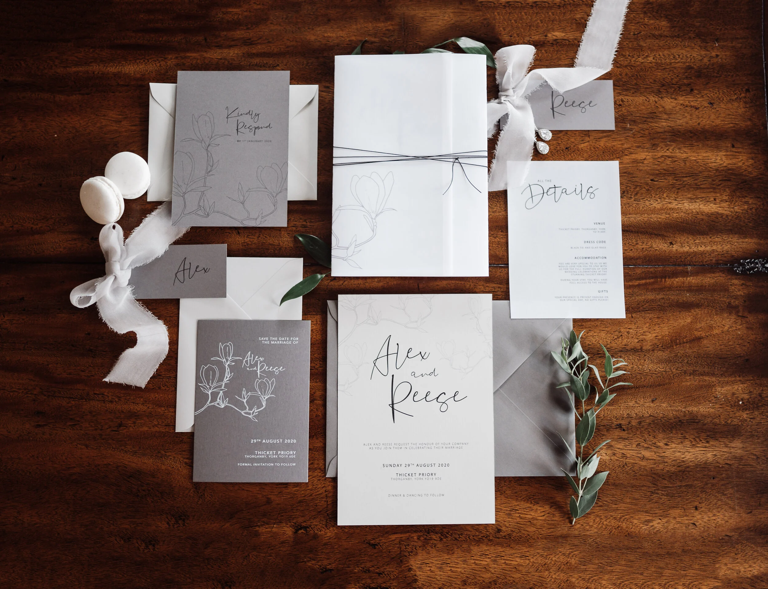Wedding invitations and stationery with a floral design, along with greenery and decorative ribbon on a wooden table.