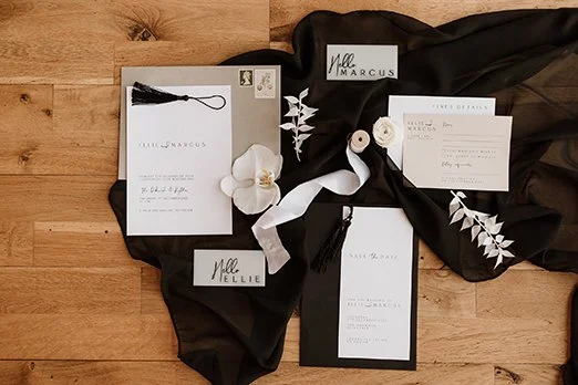 Invitation suite with black and white stationery, floral accents, and black fabric on a wooden surface.
