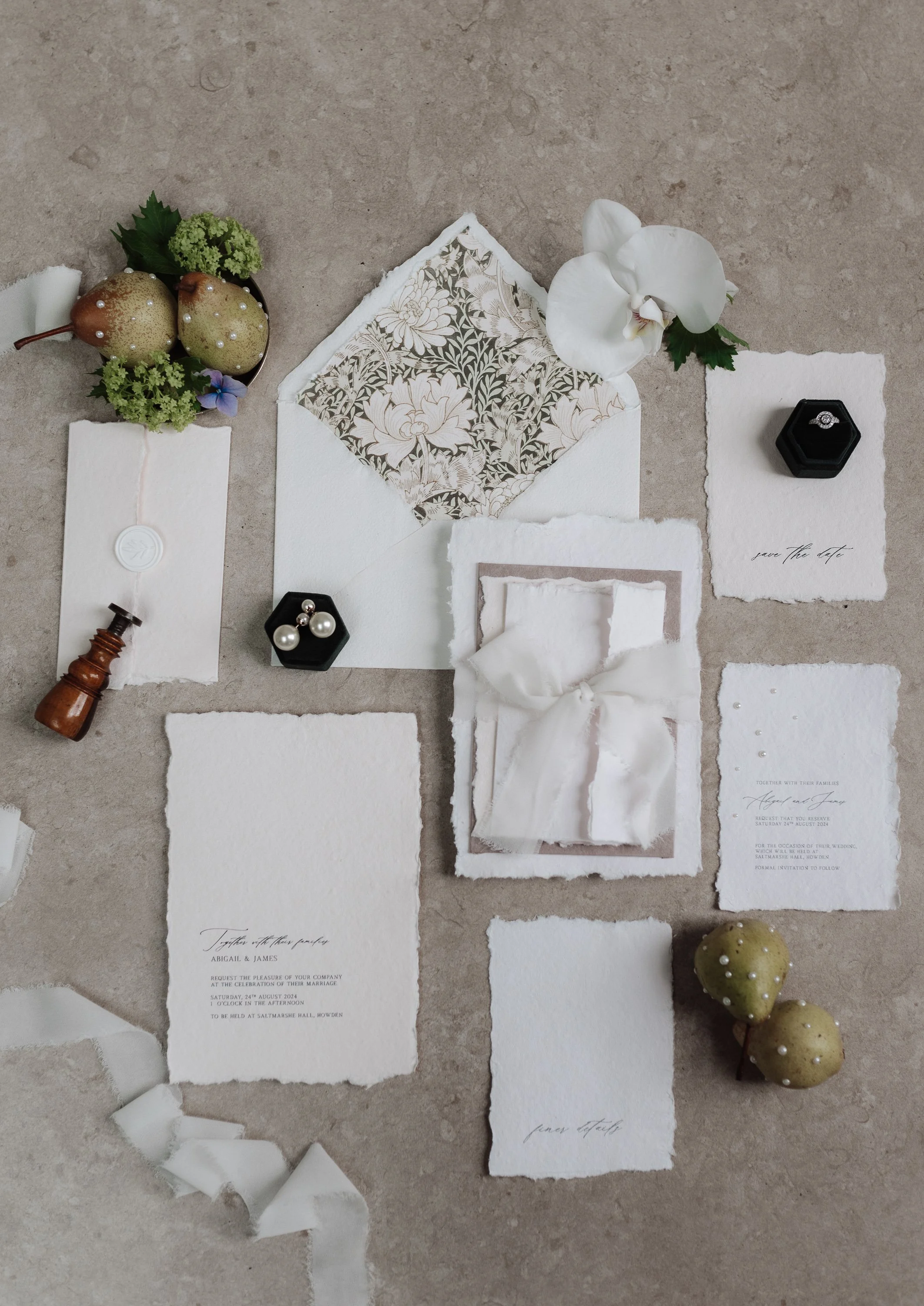 Wedding invitation suite with floral and gold accents, wedding rings, pearls, and decorative elements on a neutral background.