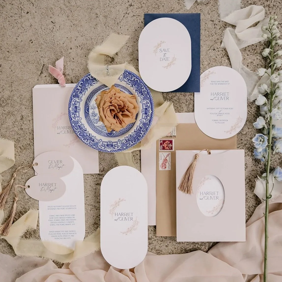 Wedding invitation suite with save the date, RSVP card, and accompanying stationery, decorated with a beige flower, cream and pink ribbons, and a floral element on the right side.