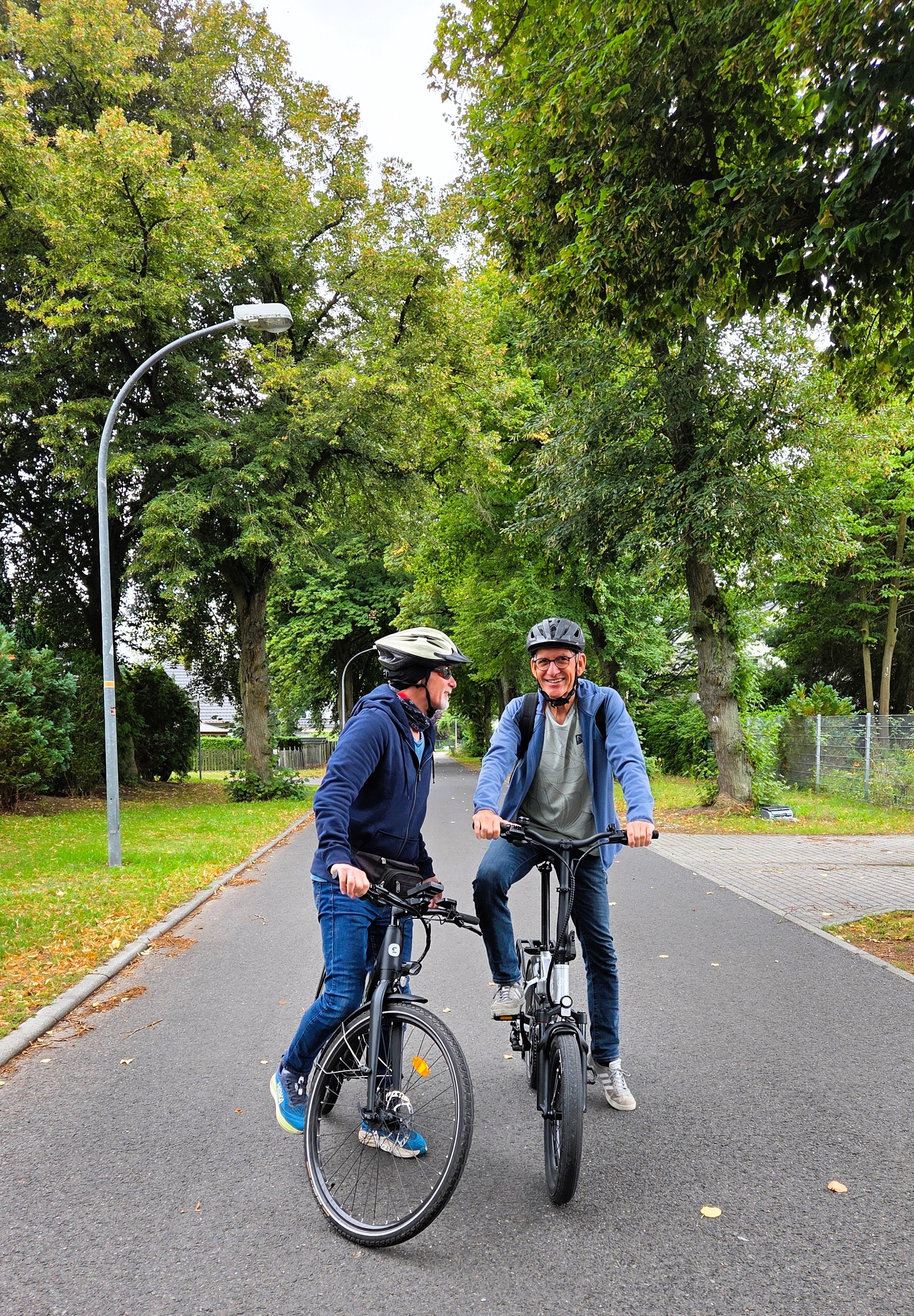 Genießen statt anstrengen – E-Bike-Test, zwei Männer mit Fahrrädern auf der Straße miteinander redend