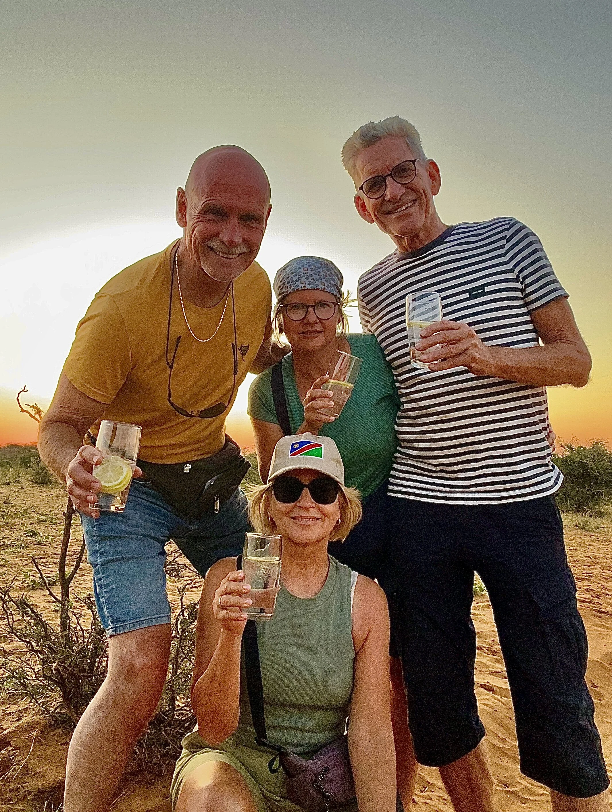 Gin-Gin-Gin, Okavango, vier Personen mit Gläsern in den Händen vor einem Sonnenuntergang