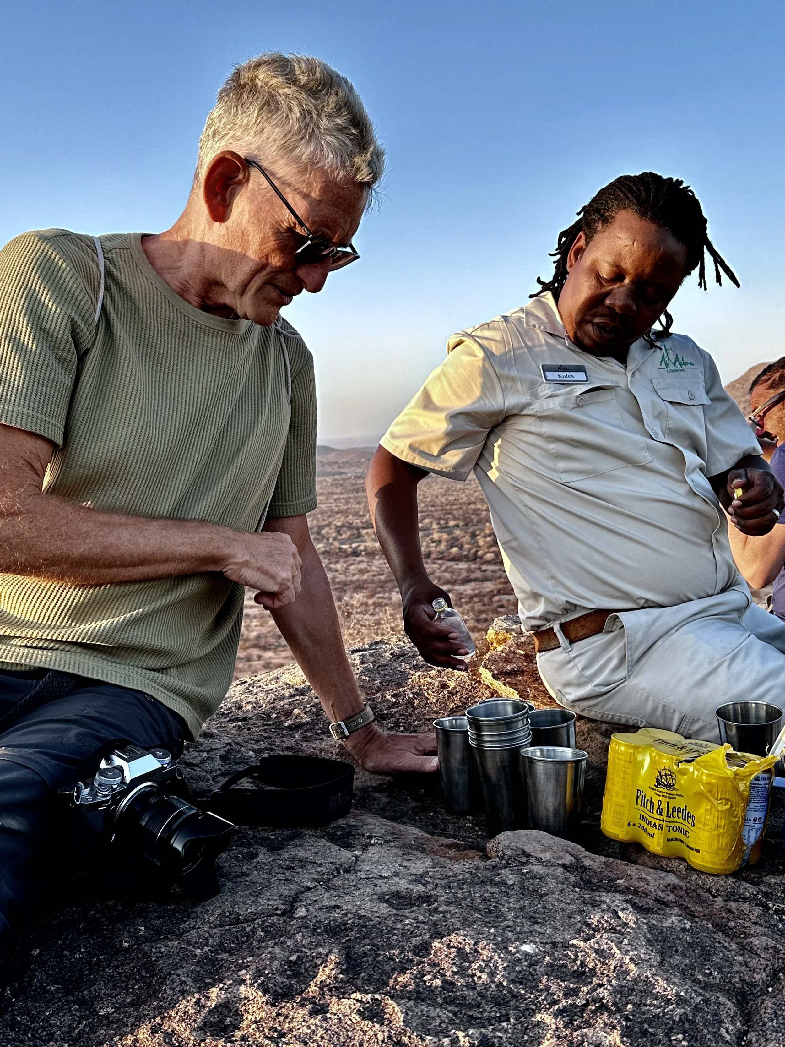 Gin-Gin-Gin, Okavango, zwei Männer auf einem Berg sitzend und Gin mit Tonic eingießend