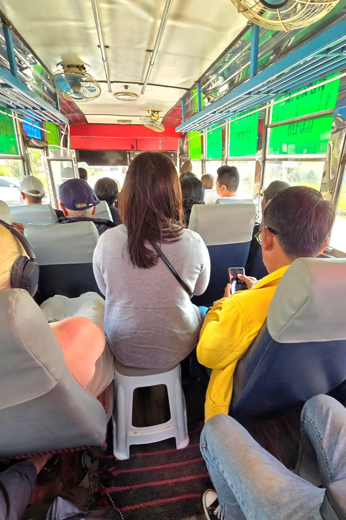 Vollbesetzter Bus, eine Frau sitzt zusätzlich auf Plastikhocker, Rundreise Laos auf eigene Faust