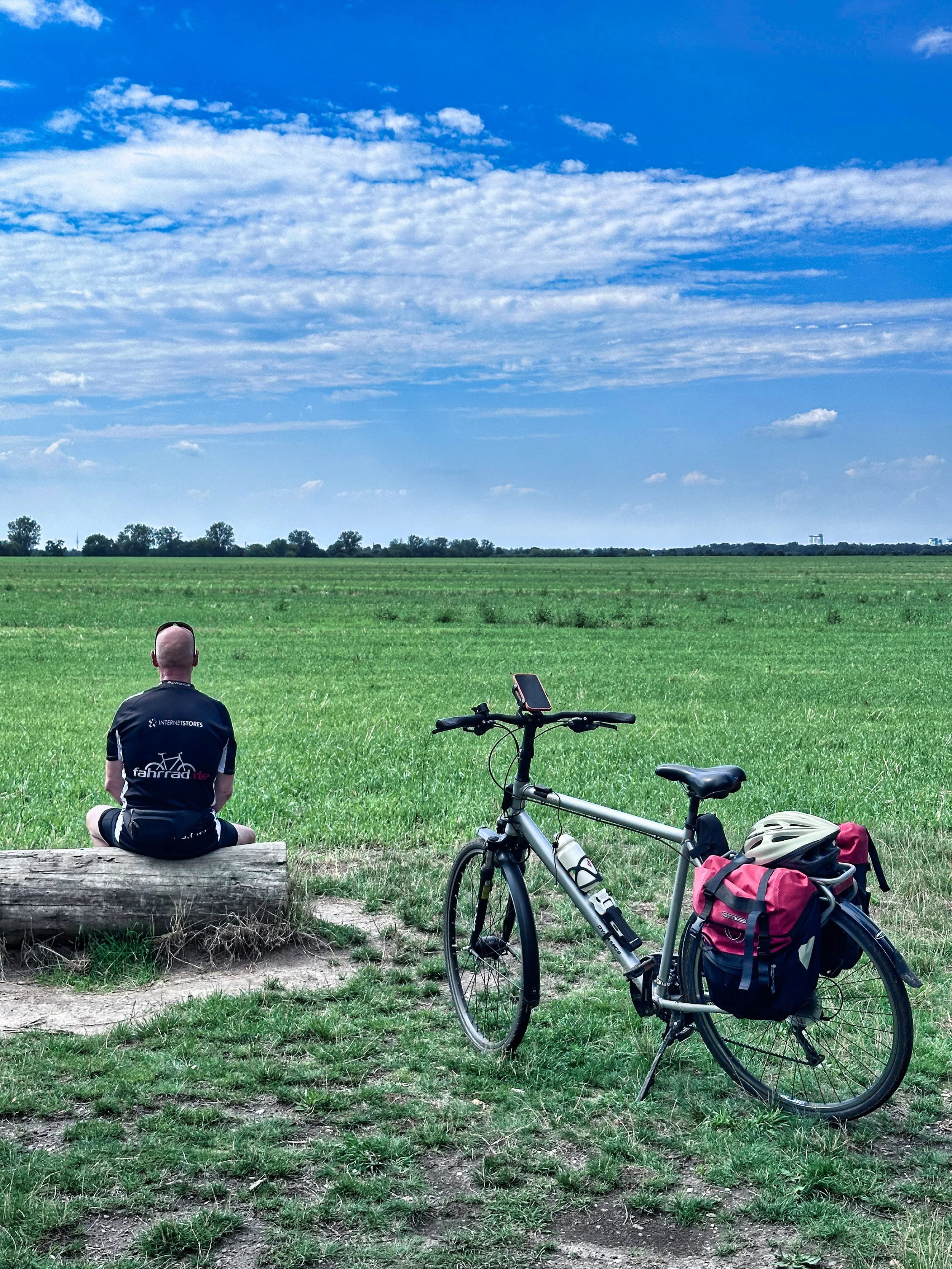 Berliner Mauerweg mit dem Fahrrad, Mann von hinten mit Fahrrad auf einem Baumstamm