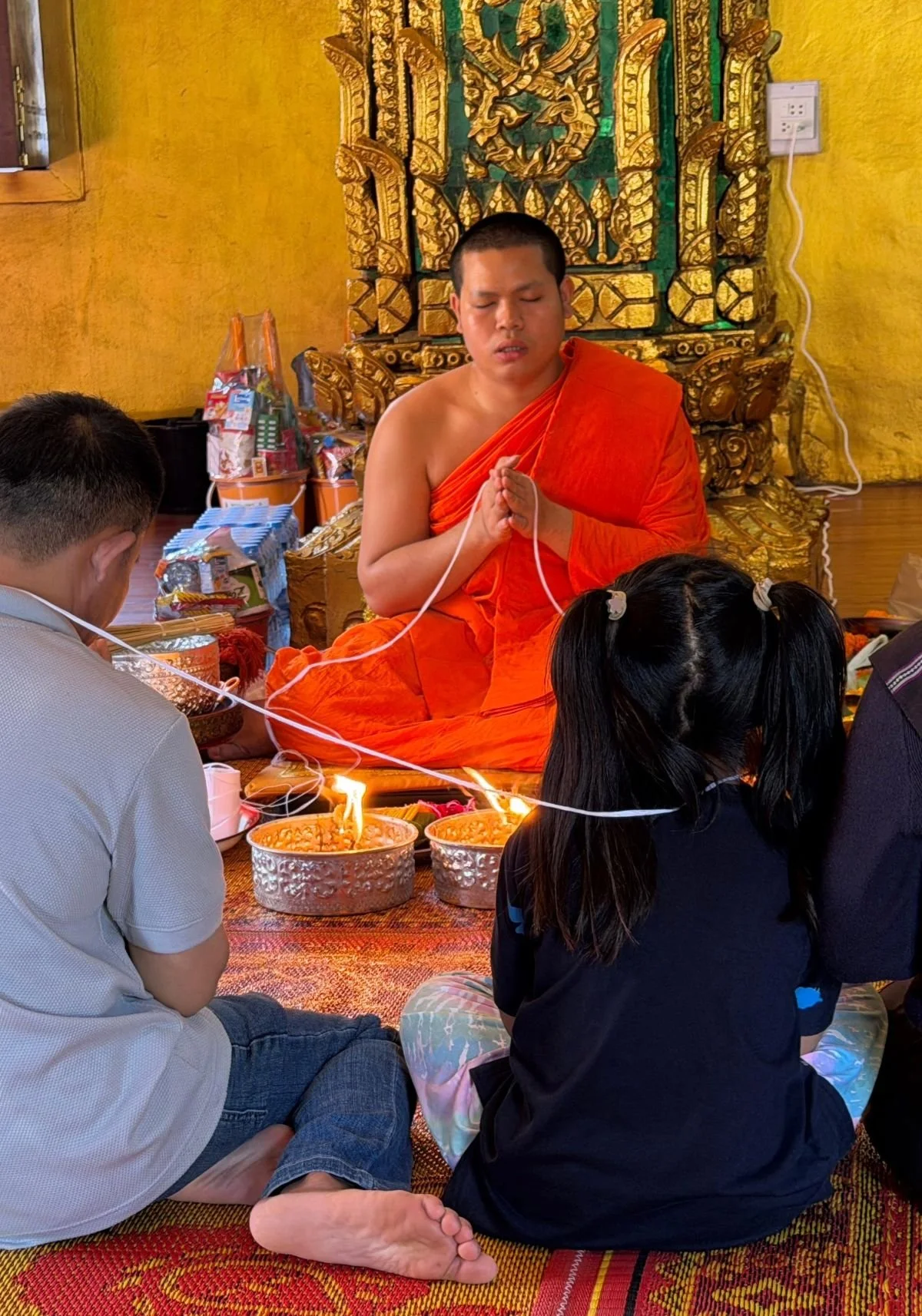 Laos - Rundreise auf eigene Faust - Mönch meditiert im Tempel, mit einem Wollfaden mit den Gläubigen verbunden