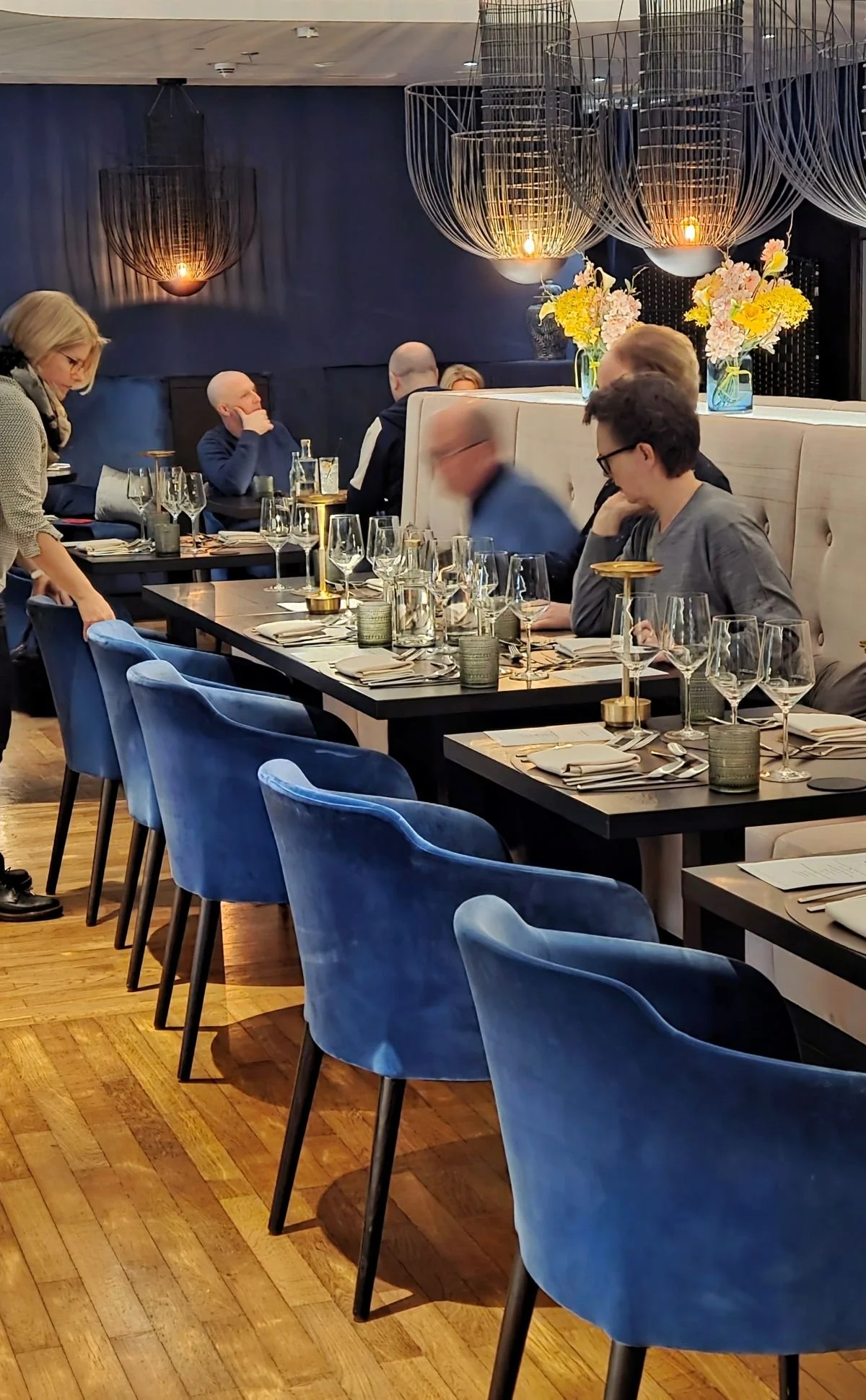 Besucher setzen sich an Tisch mit blauen Polsterstühlen - Morgenpost-Menü April 2026 - Heritage