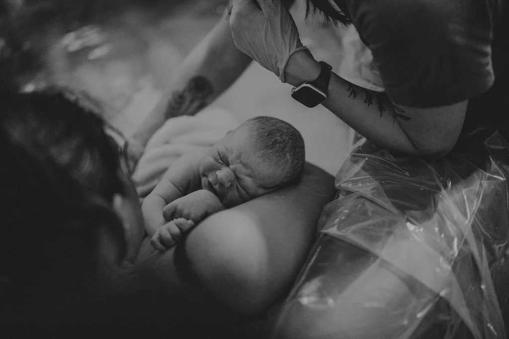 Woman holding newborn baby while midwife checks in