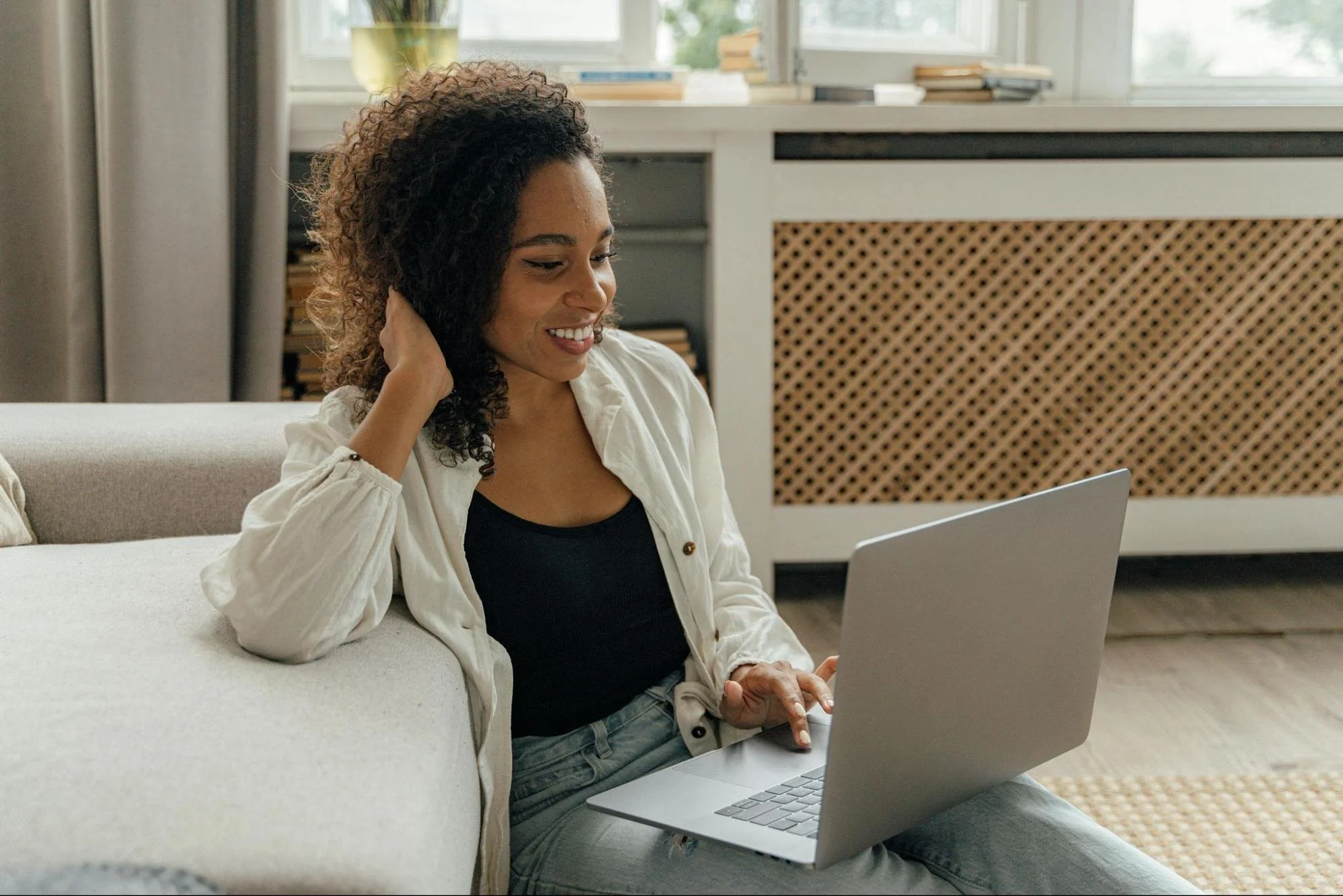 Woman wear light colored blouse looking at computer smiling.