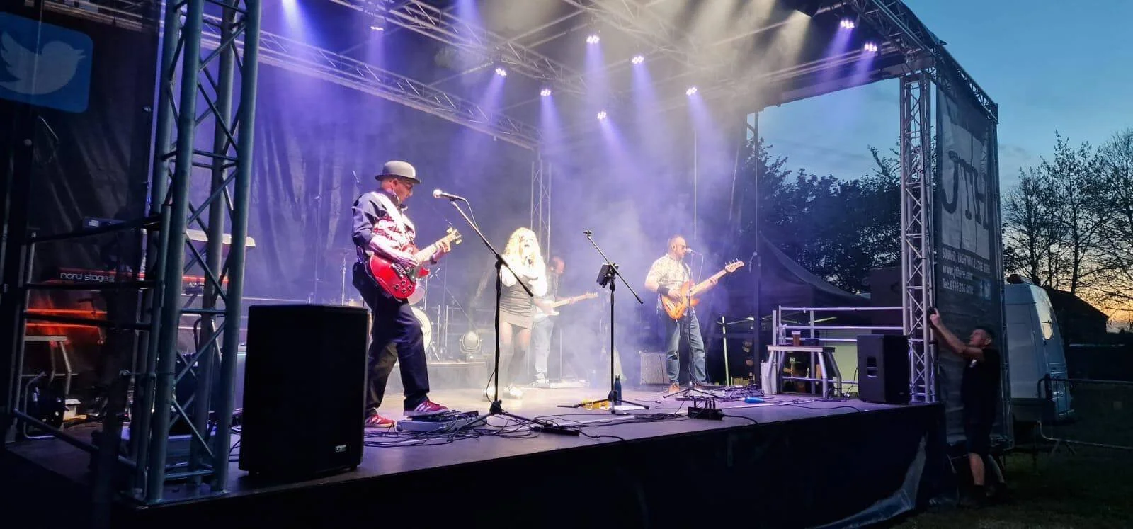 Live band performing on covered outdoor stage with stage lighting and PA sound system