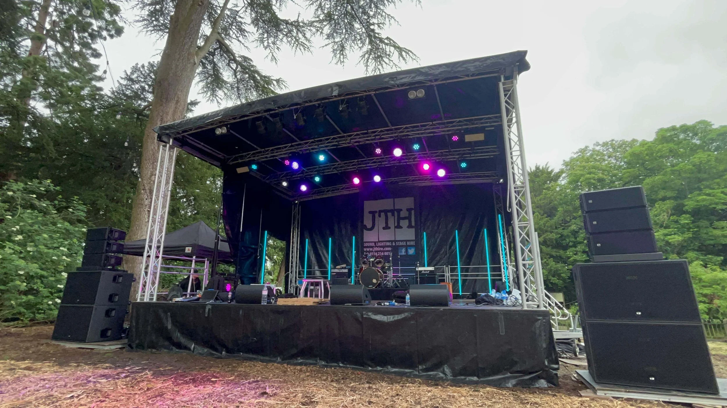 Large covered festival stage hire with side speaker stacks set up outdoors in park