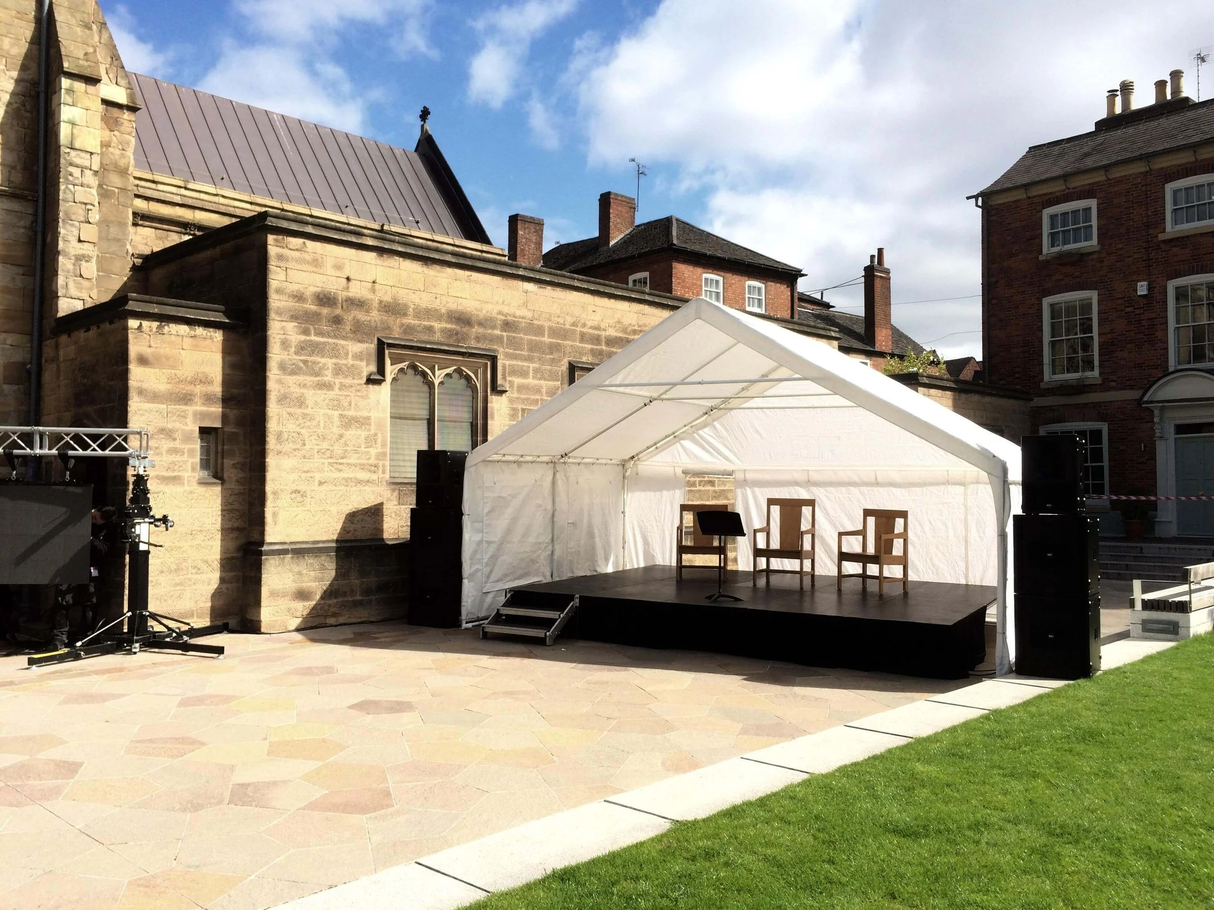 Small outdoor event stage setup under white canopy marquee outside stone building venue