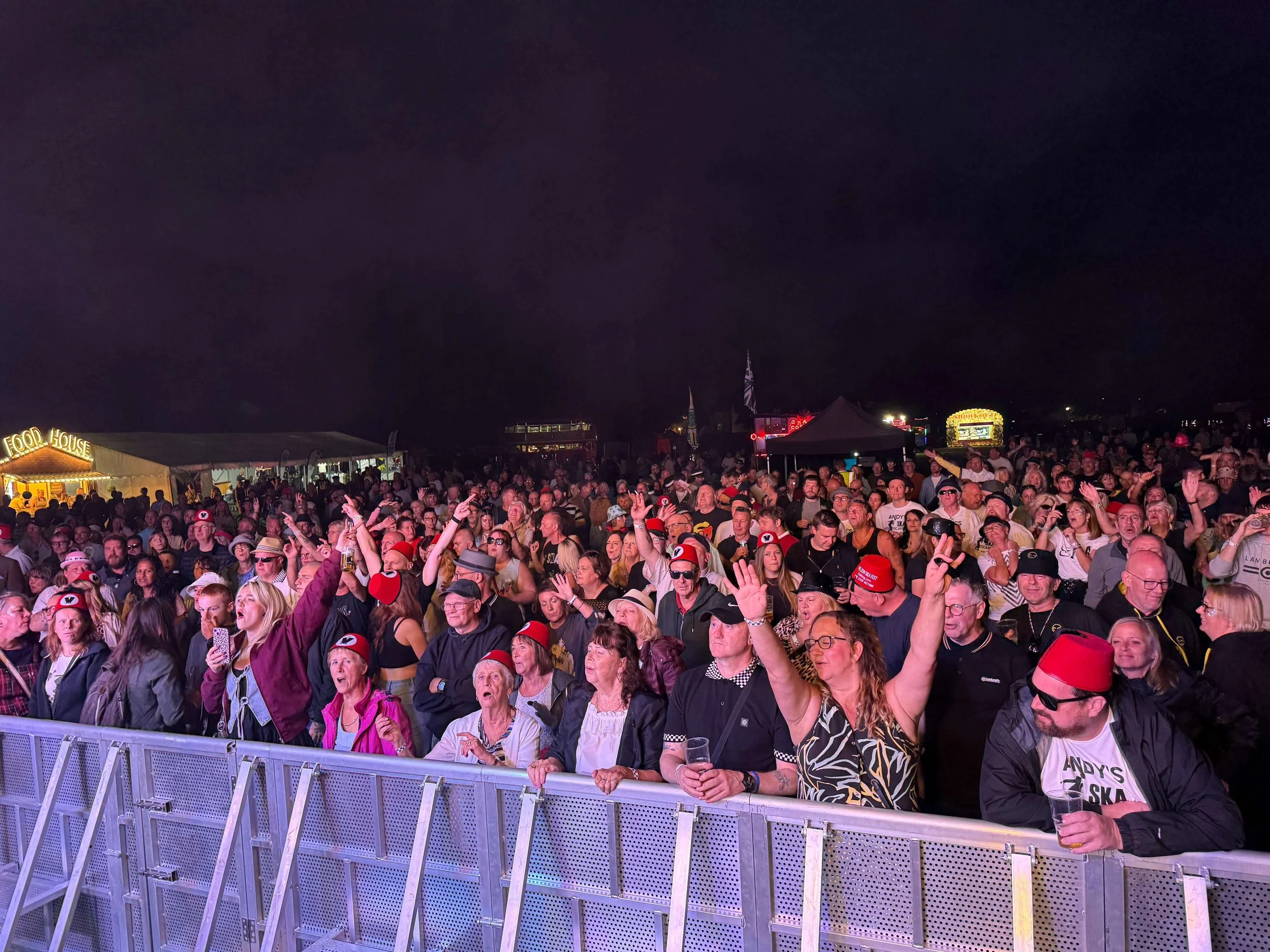 Large outdoor concert crowd behind silver crowd control safety barriers at night