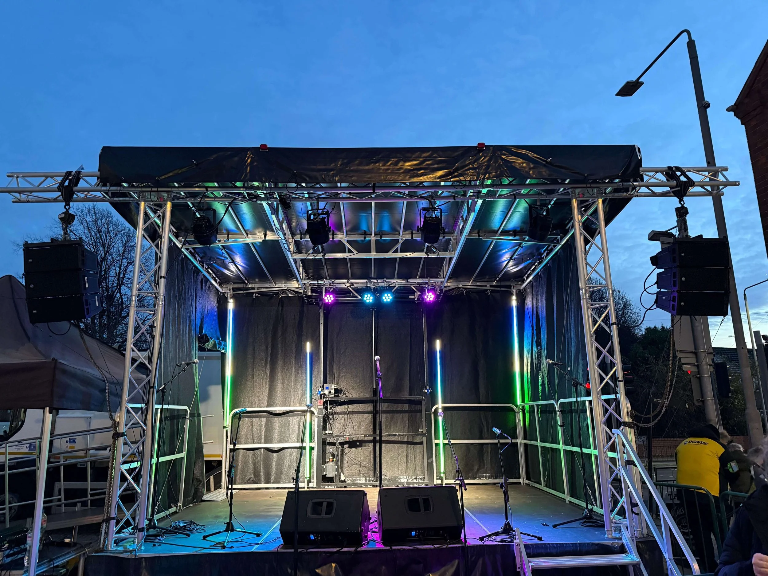 Small outdoor event stage featuring professional overhead stage lighting truss and speakers