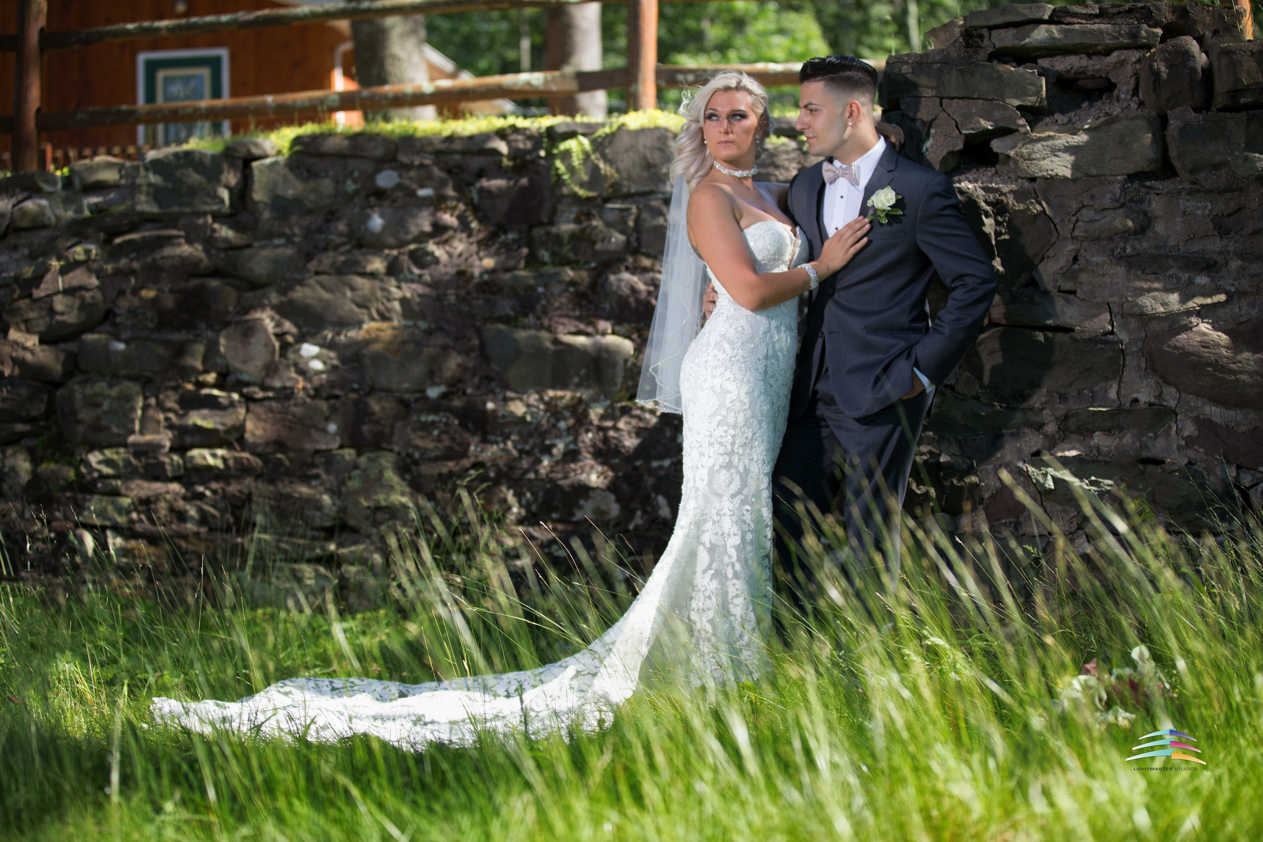 wedding-couple-in-front-of rock-wall-with-blowing-green-white-wedding-dress-form-fitting-and-gray-tuxedo-Trout-Lake-Inn-Summer-Project-Lightmaster-studios-.jpg