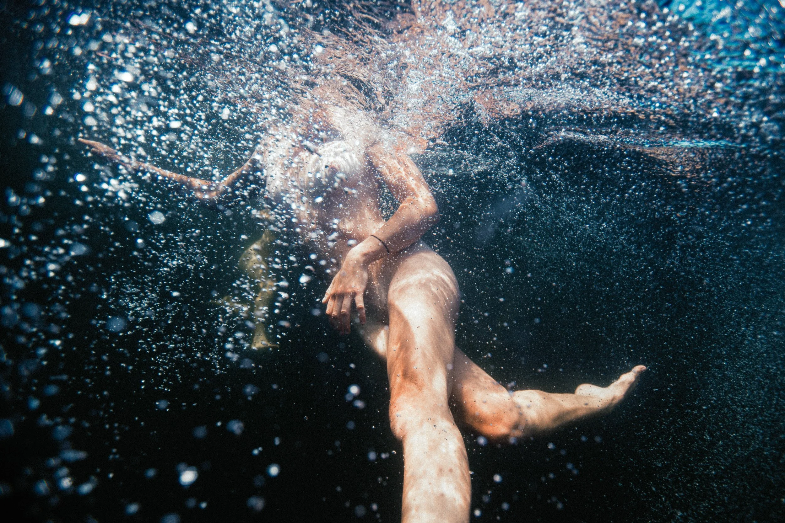 A person swimming underwater surrounded by bubbles, with their knees bent and arms extended.