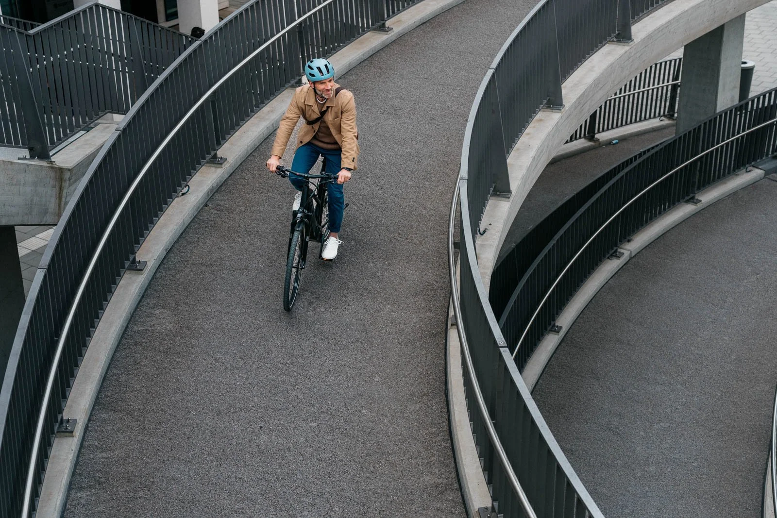 A man wearing a blue helmet riding a black bicycle on an outdoor pathway with curved metal railings.