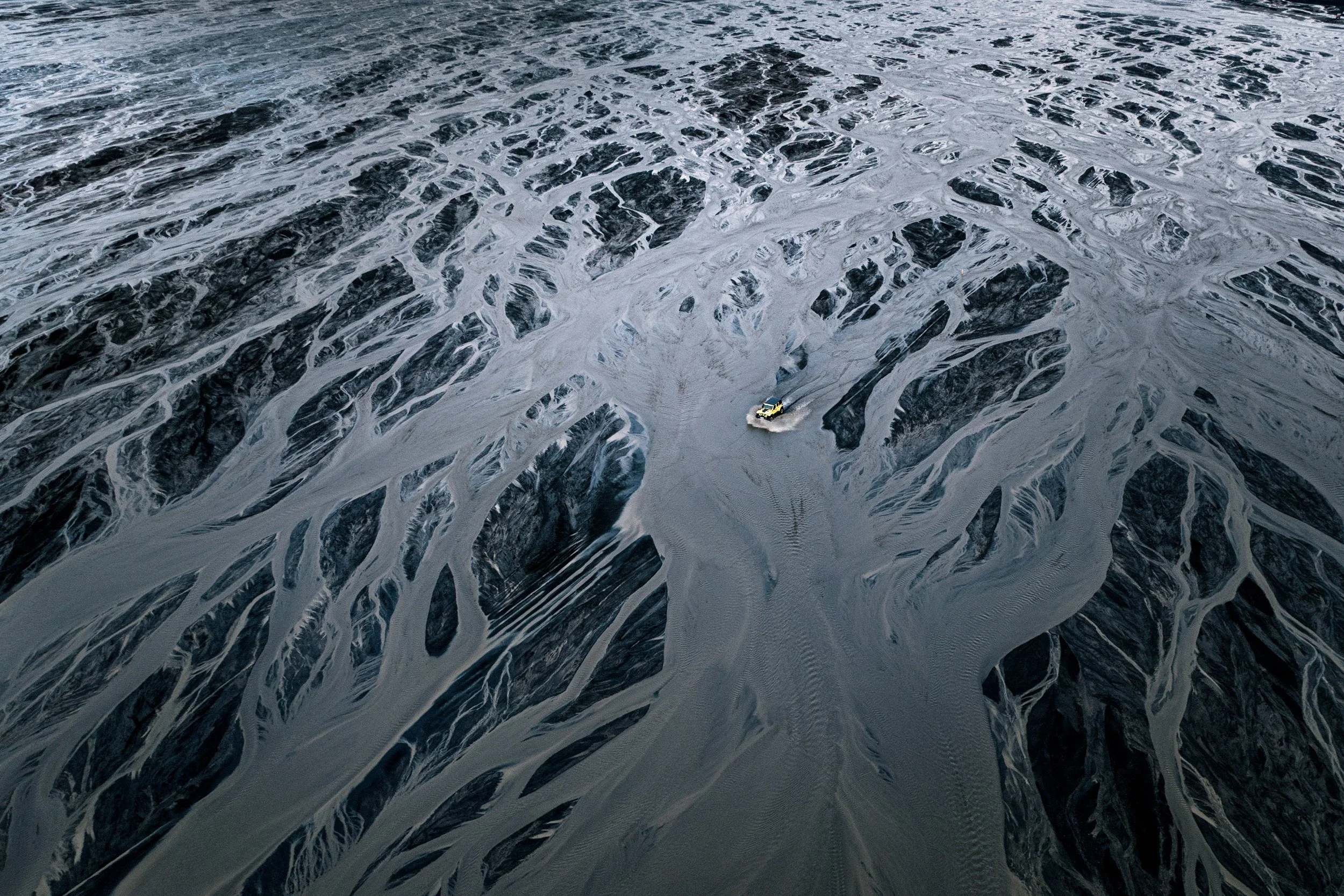 Aerial view of a large open salt flat with white salt formations and a small vehicle driving across the surface.