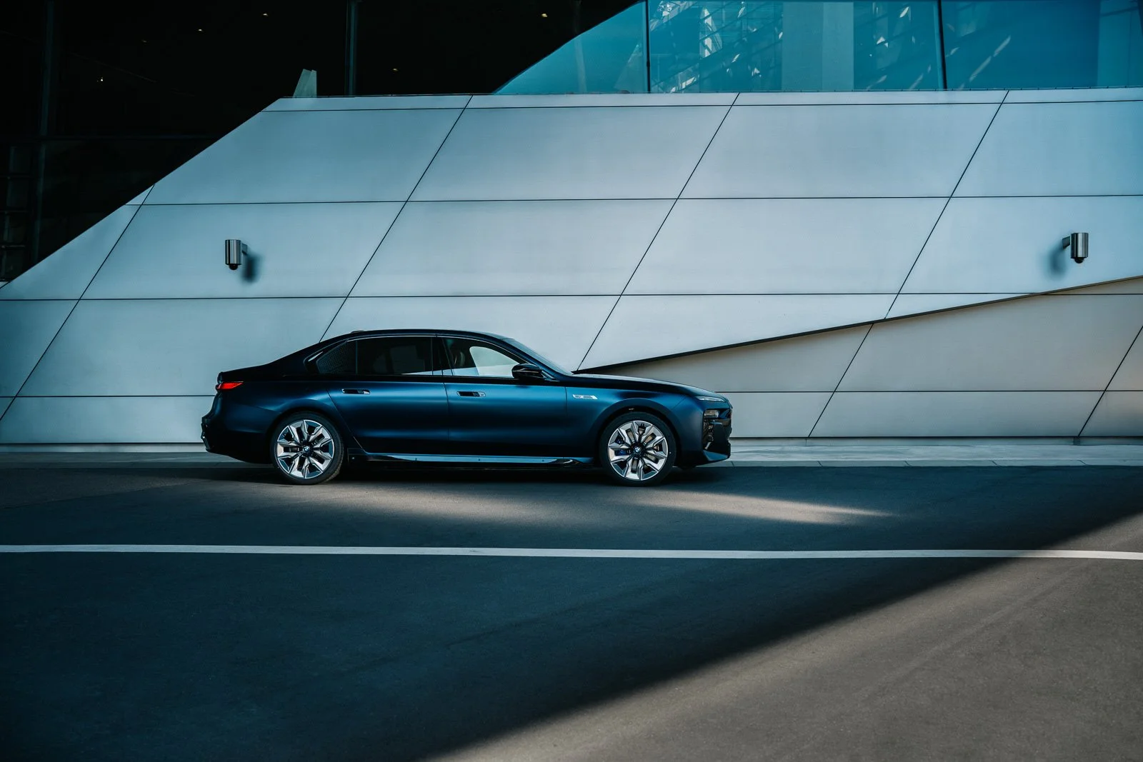 A sleek black luxury sedan parked along a modern building with minimalist exterior design in an urban setting.