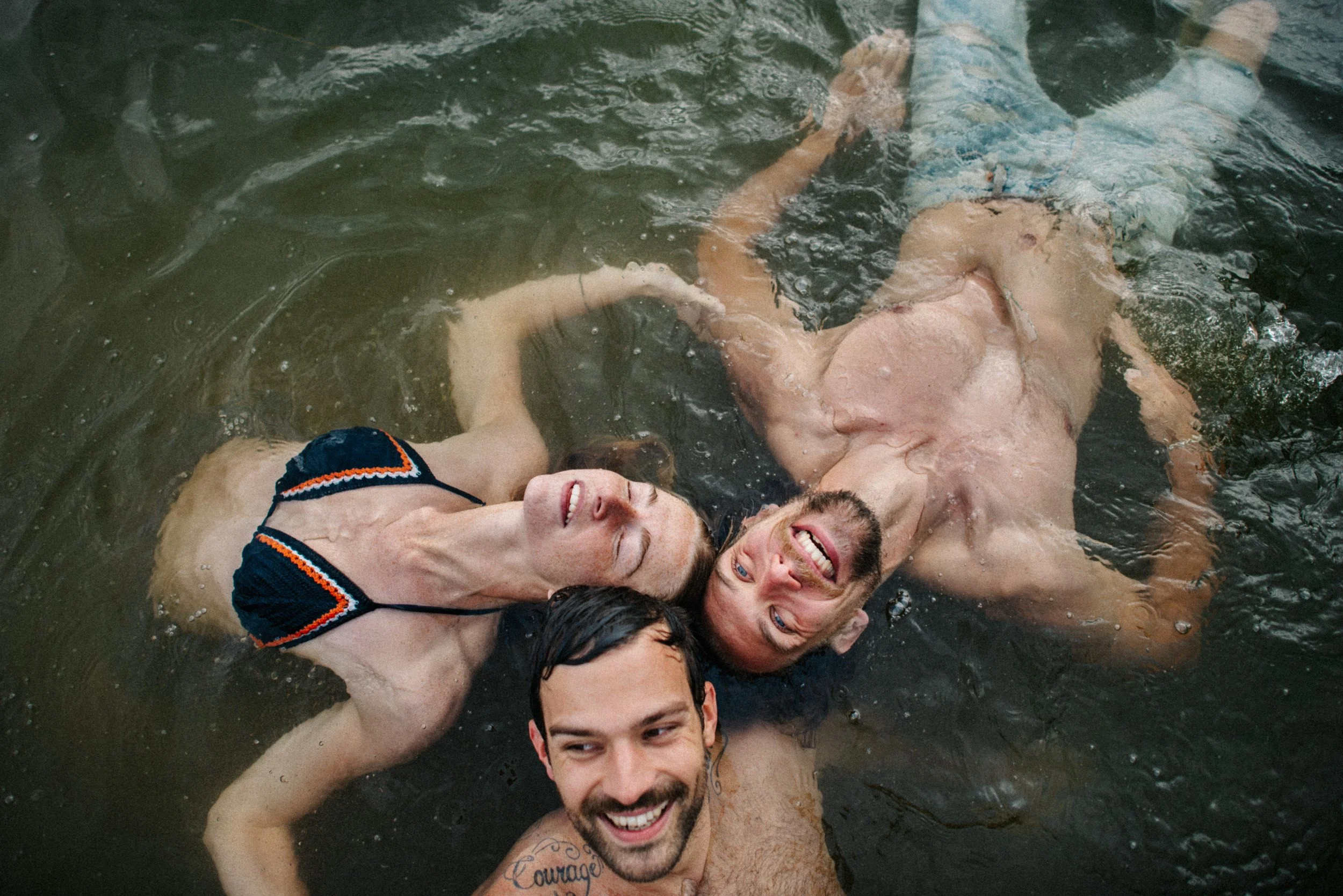 Three people, two men and a woman, enjoying a swim in water, smiling and relaxing.
