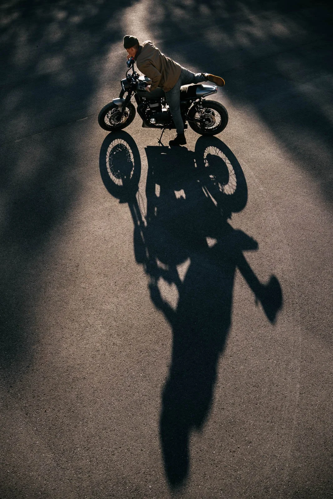 A man riding a motorcycle on an asphalt road, casting a long shadow in the sunlight.