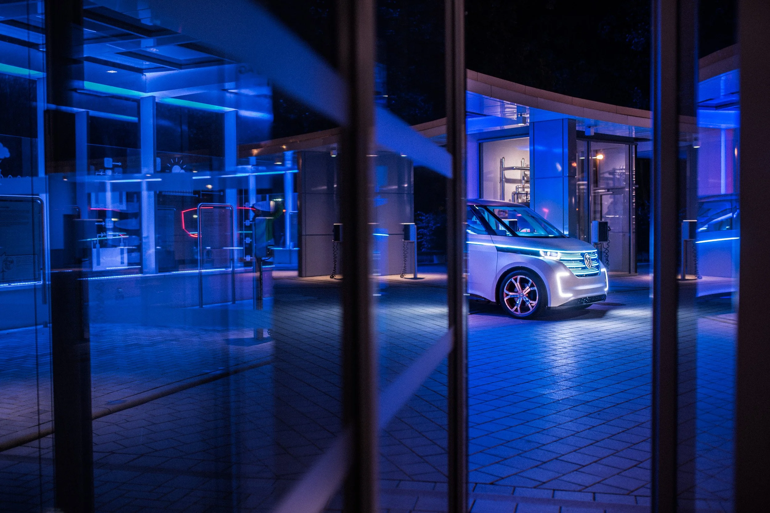 An electric vehicle charging station at night with a modern silver car plugged in, illuminated by blue LED lights.