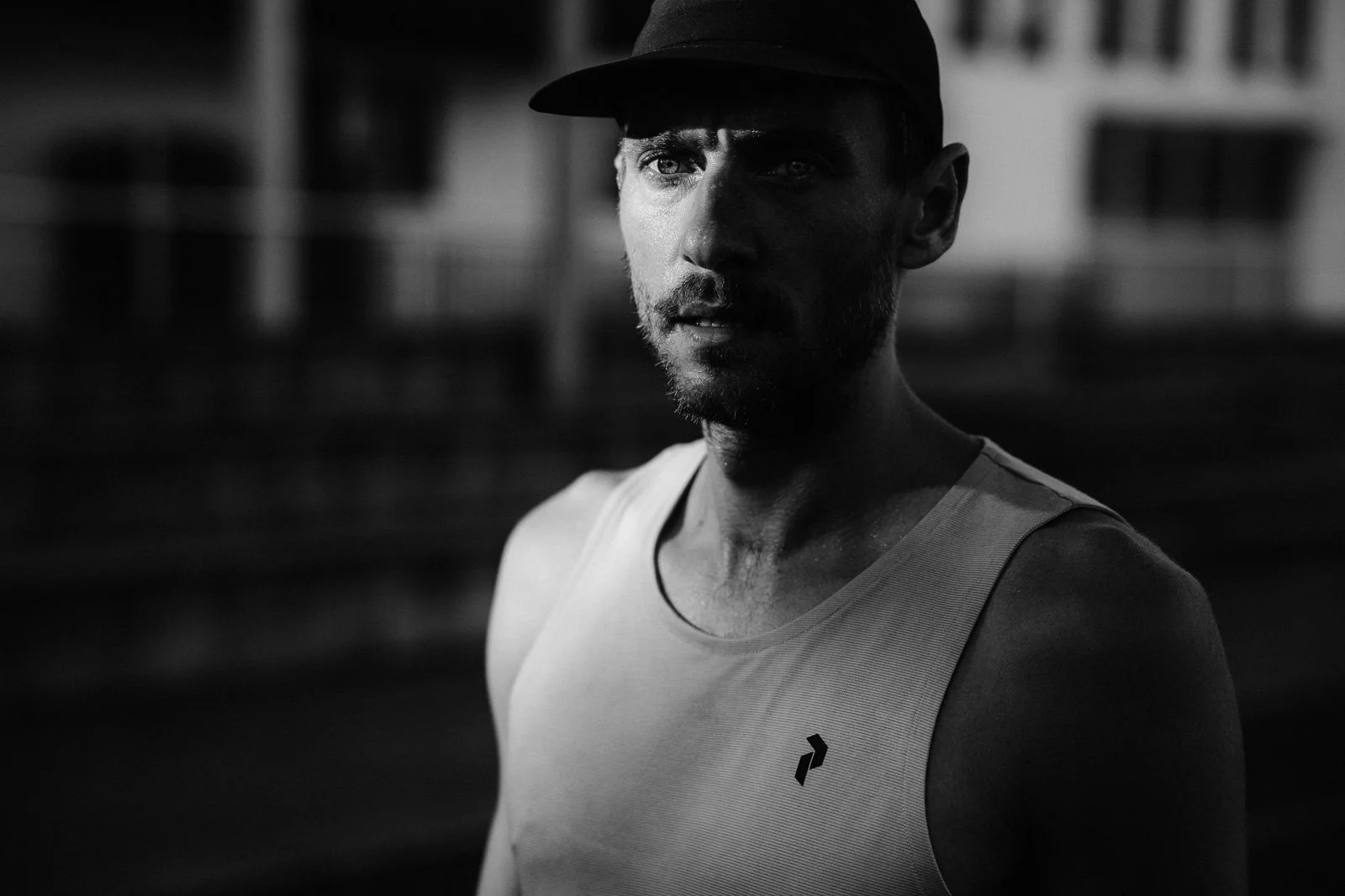 A black-and-white photo of a man wearing a baseball cap and athletic tank top, outdoors on a sunny day.