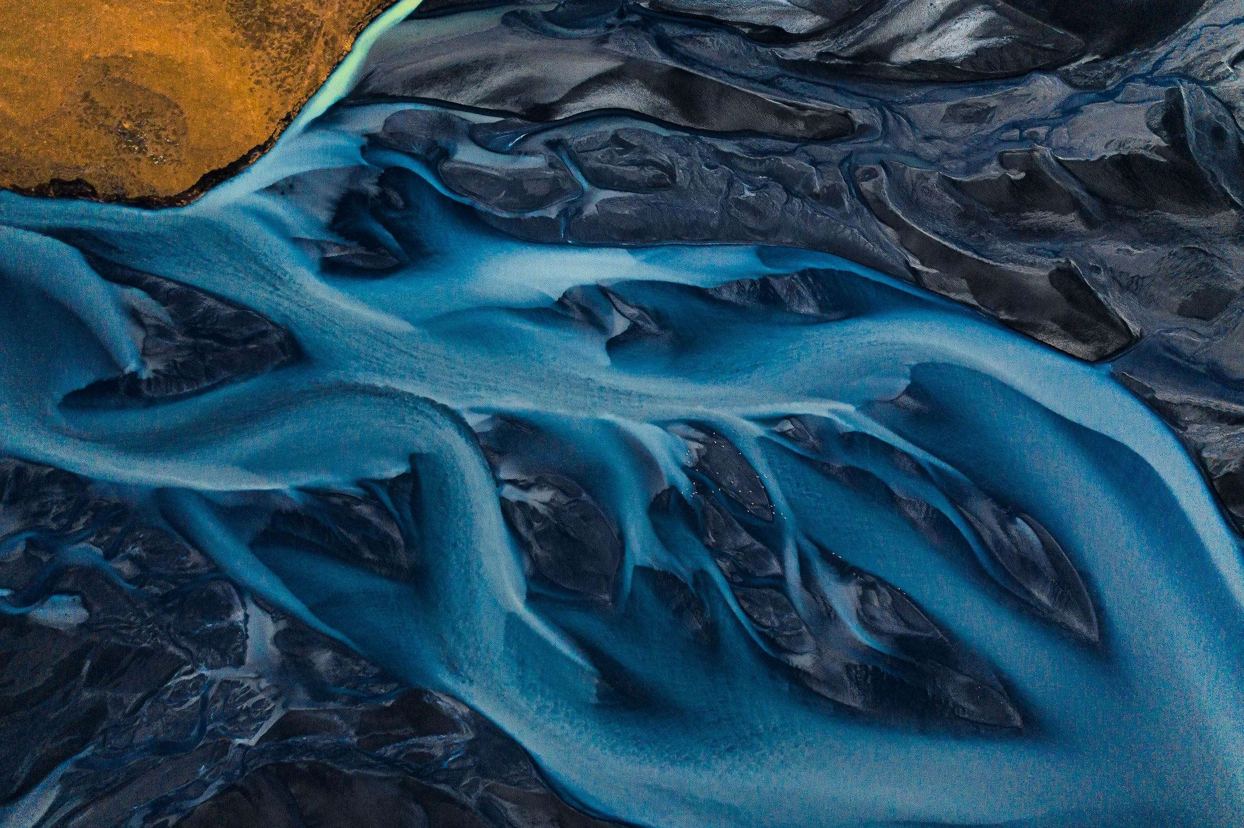 Aerial view of a glacier with blue ice flowing between dark rocky terrain.
