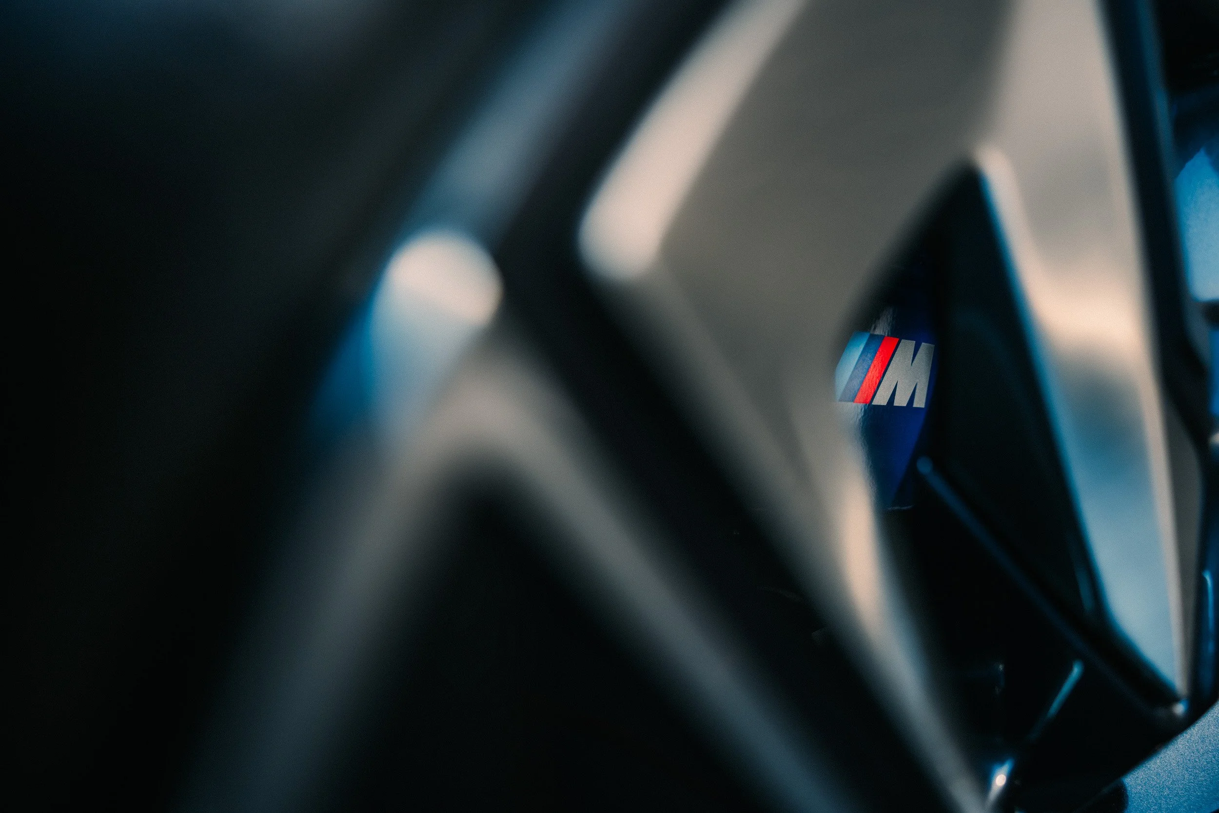 Close-up of a car's steering wheel with the BMW M badge partially visible in the background.