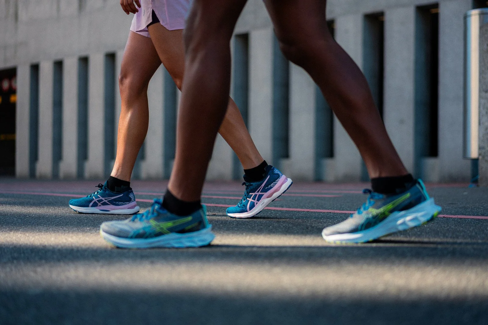Close-up of two people in athletic shoes and shorts preparing for a run on an outdoor track.