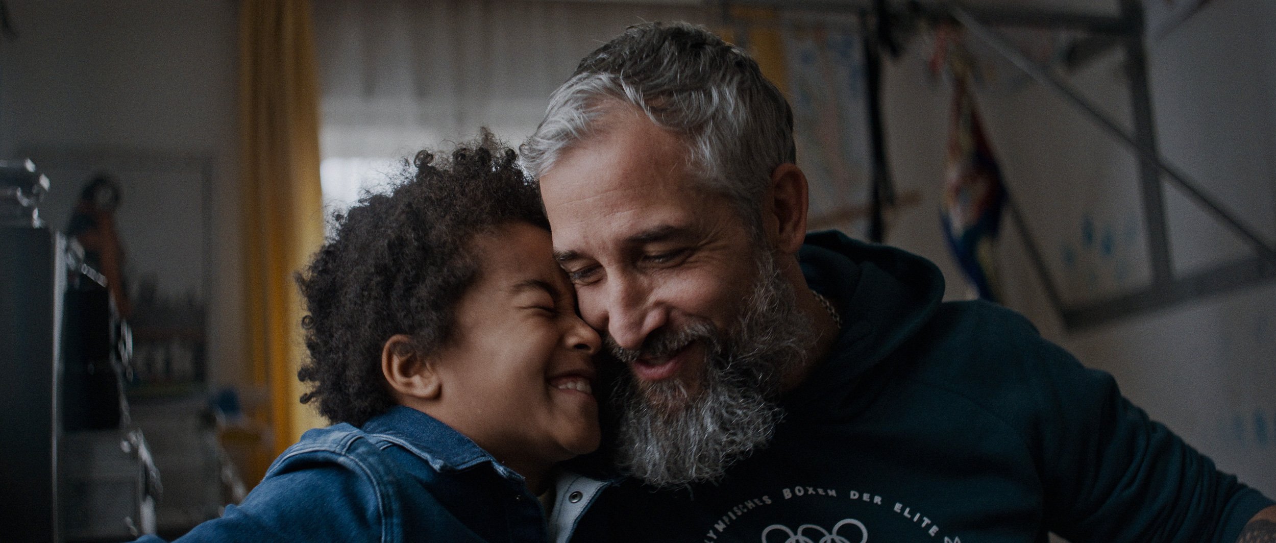 A young boy and an older man are smiling and leaning their foreheads together, showing affection and happiness.