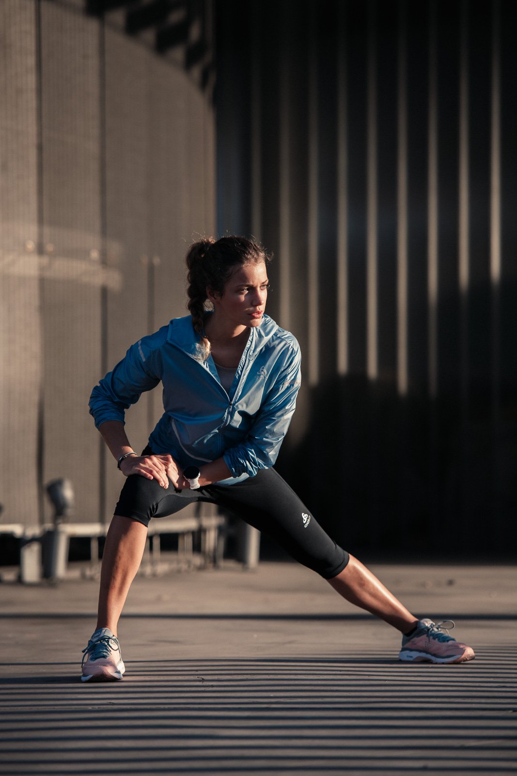 A young woman in athletic clothing stretching outdoors in the early morning or late afternoon sunlight.