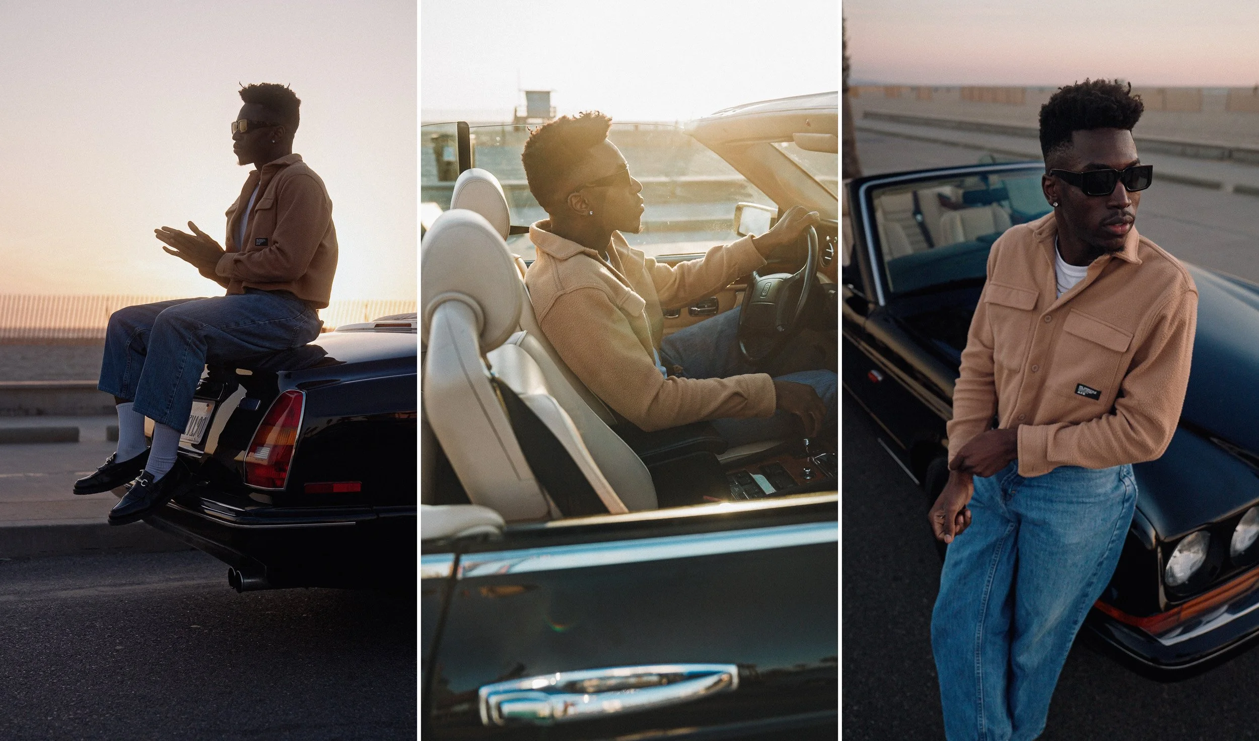A young man in sunglasses and a beige jacket posing next to a black vintage car during sunset