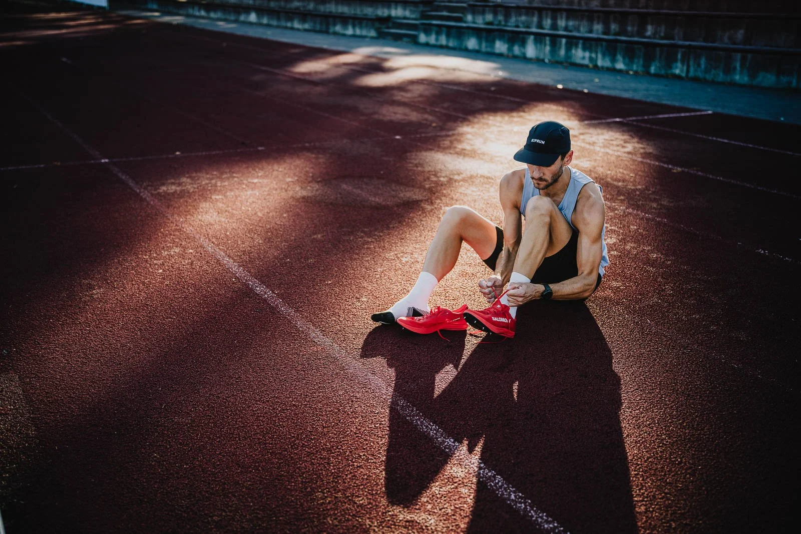 A male athlete tying his red running shoes on a running track during sunset.