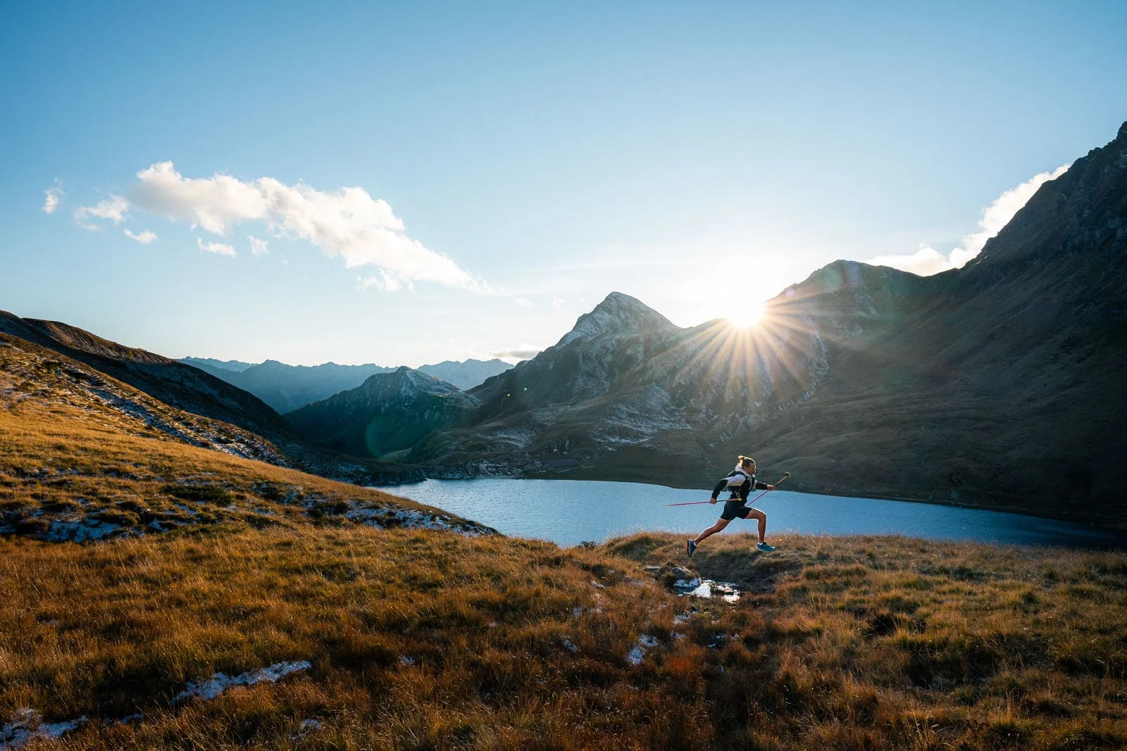 A person running on a trail near a mountain lake at sunrise with mountains in the background.