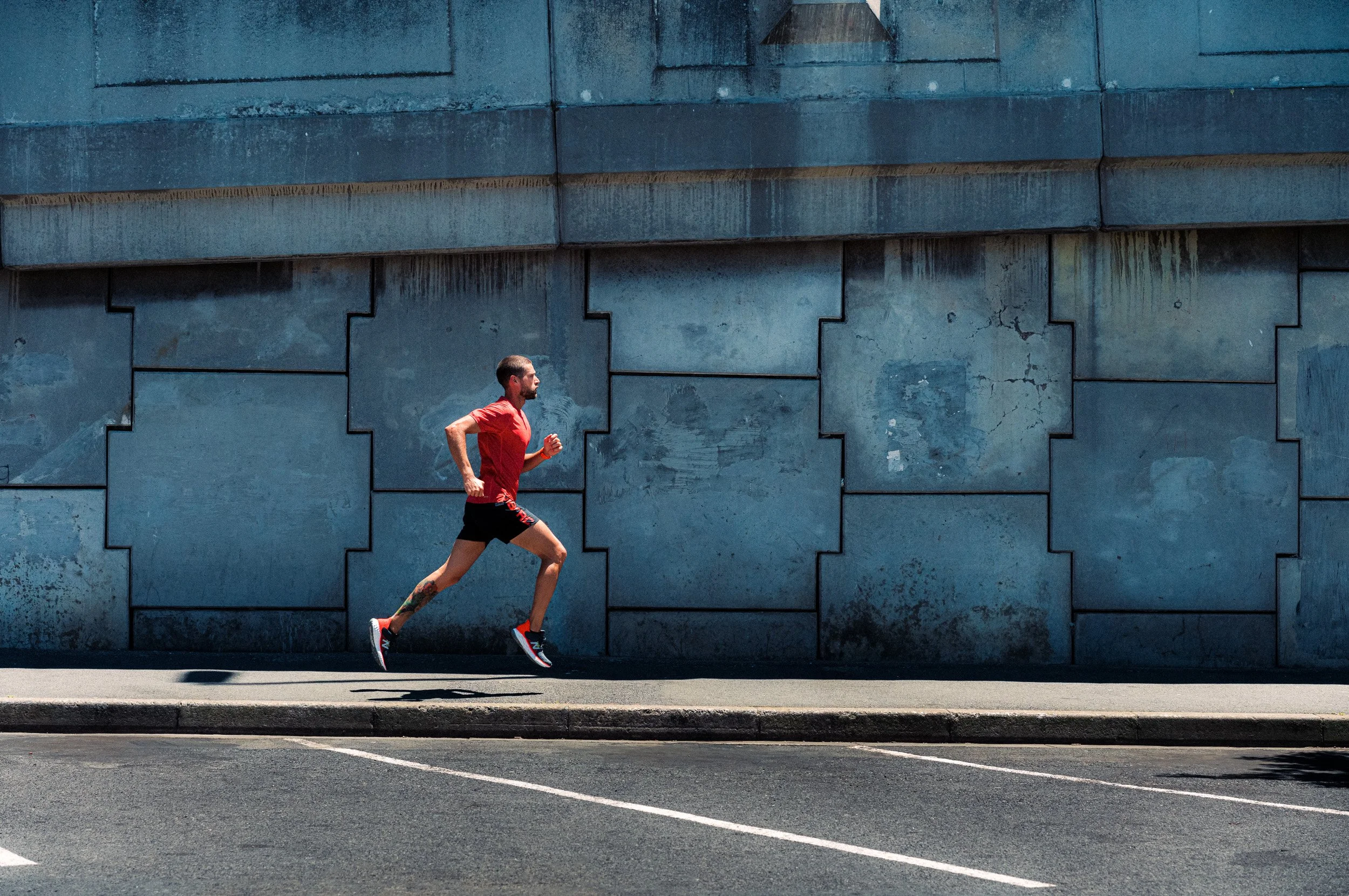 A man with a beard running on the sidewalk next to a blue concrete wall.