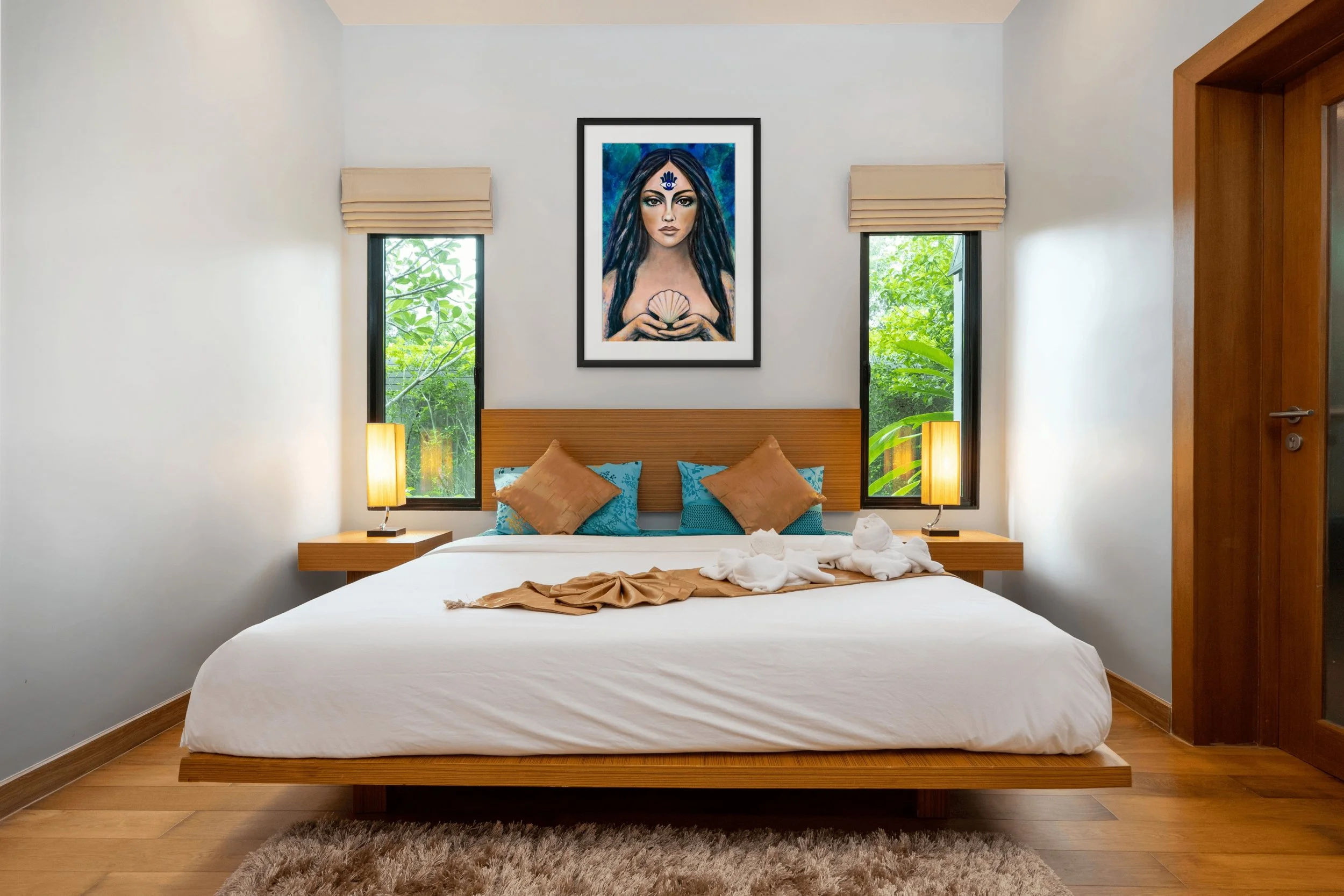 Blue goddess portrait wall art hanging above a bed in a coastal bedroom with mystical feminine details and calming ocean-inspired decor.
