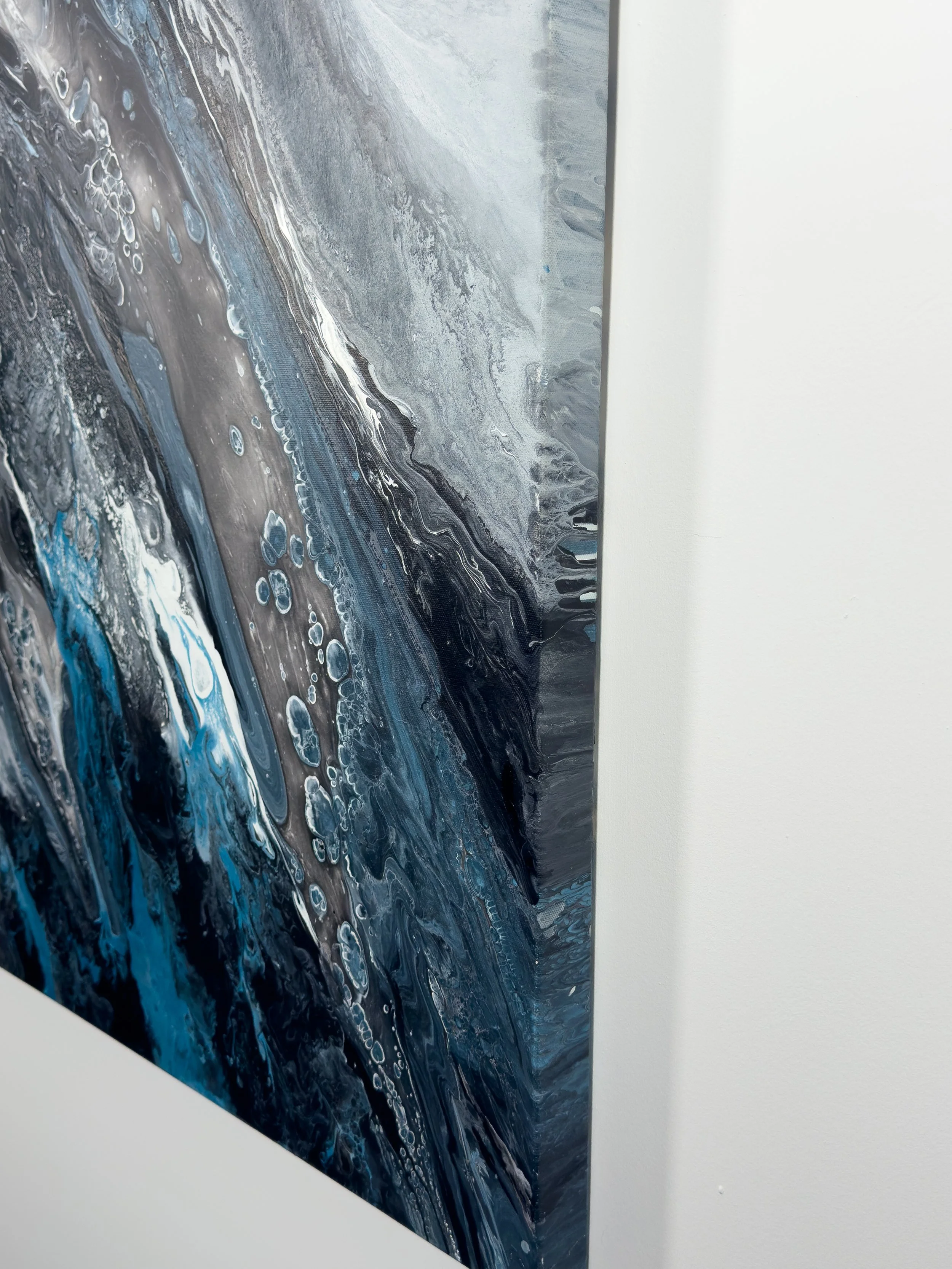 Close-up side view of a large abstract acrylic canvas featuring textured black, charcoal, silver, and electric blue flowing paint details and dimensional gallery-wrapped edges.