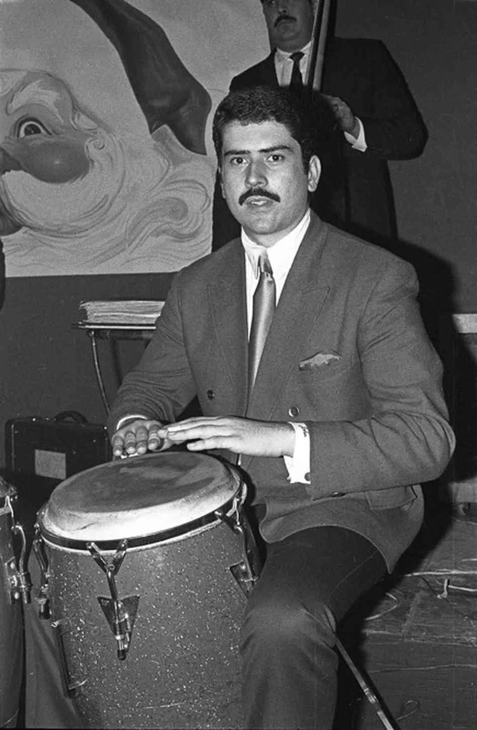 A young Johnny "Dandy" Rodríguez in a suit, playing a conga