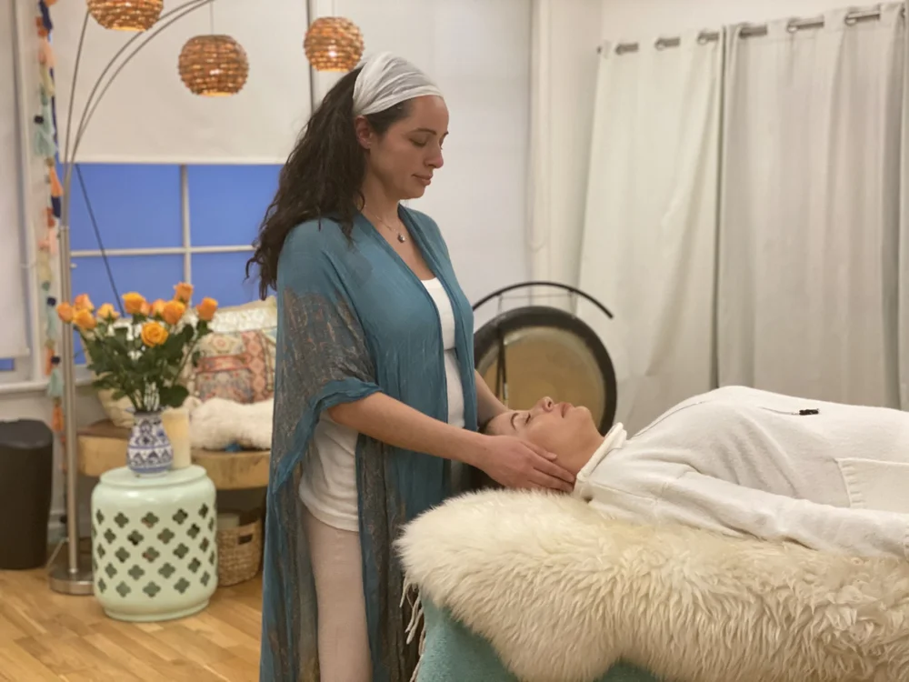 A reiki session at Atma Yoga: the practitioner's hands cradling a client's head, a gong on its stand behind